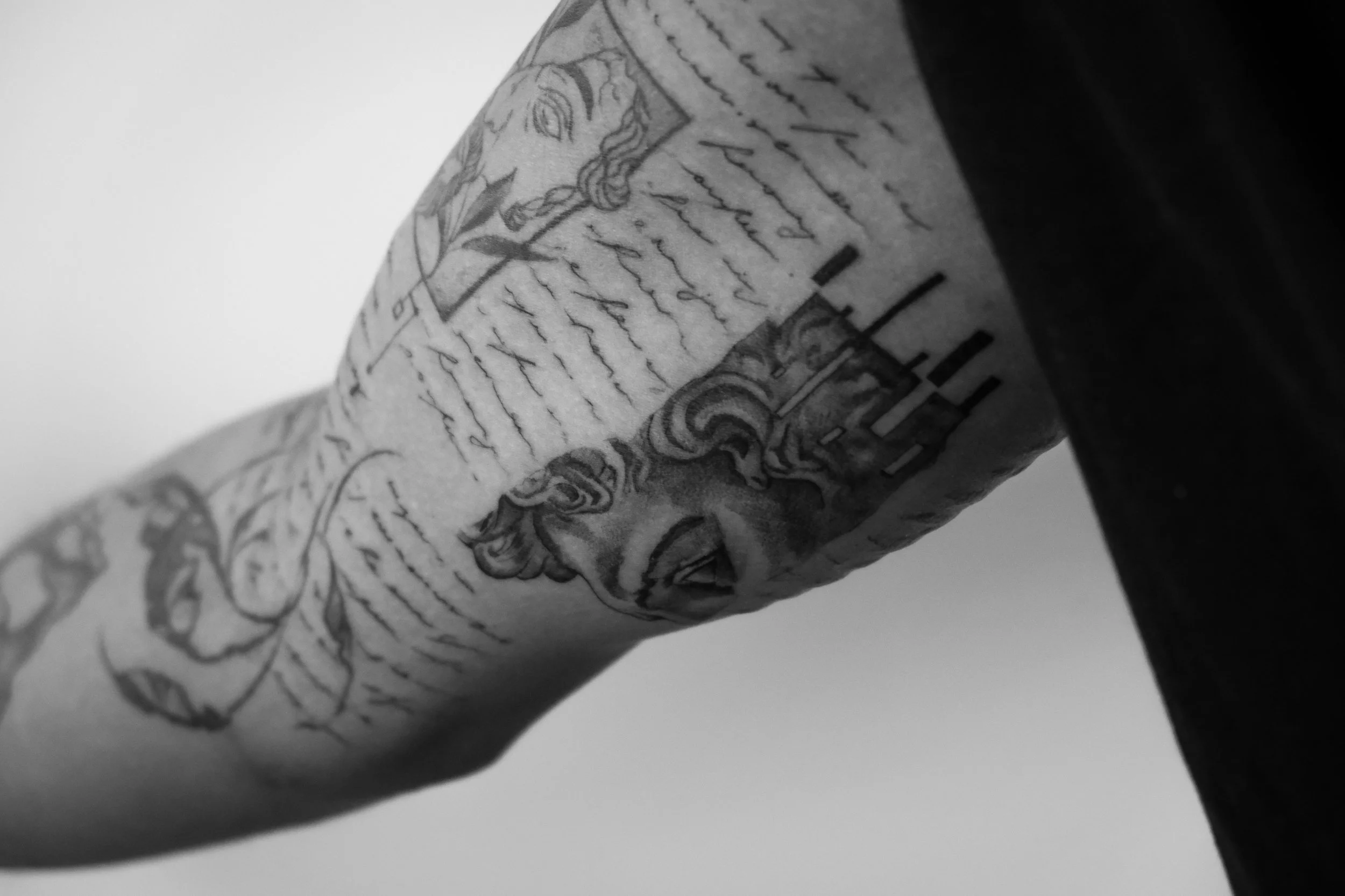 Schwarze und weiße Tätowierung eines menschlichen Armes, die ein Porträt eines Mannes und Text enthält.