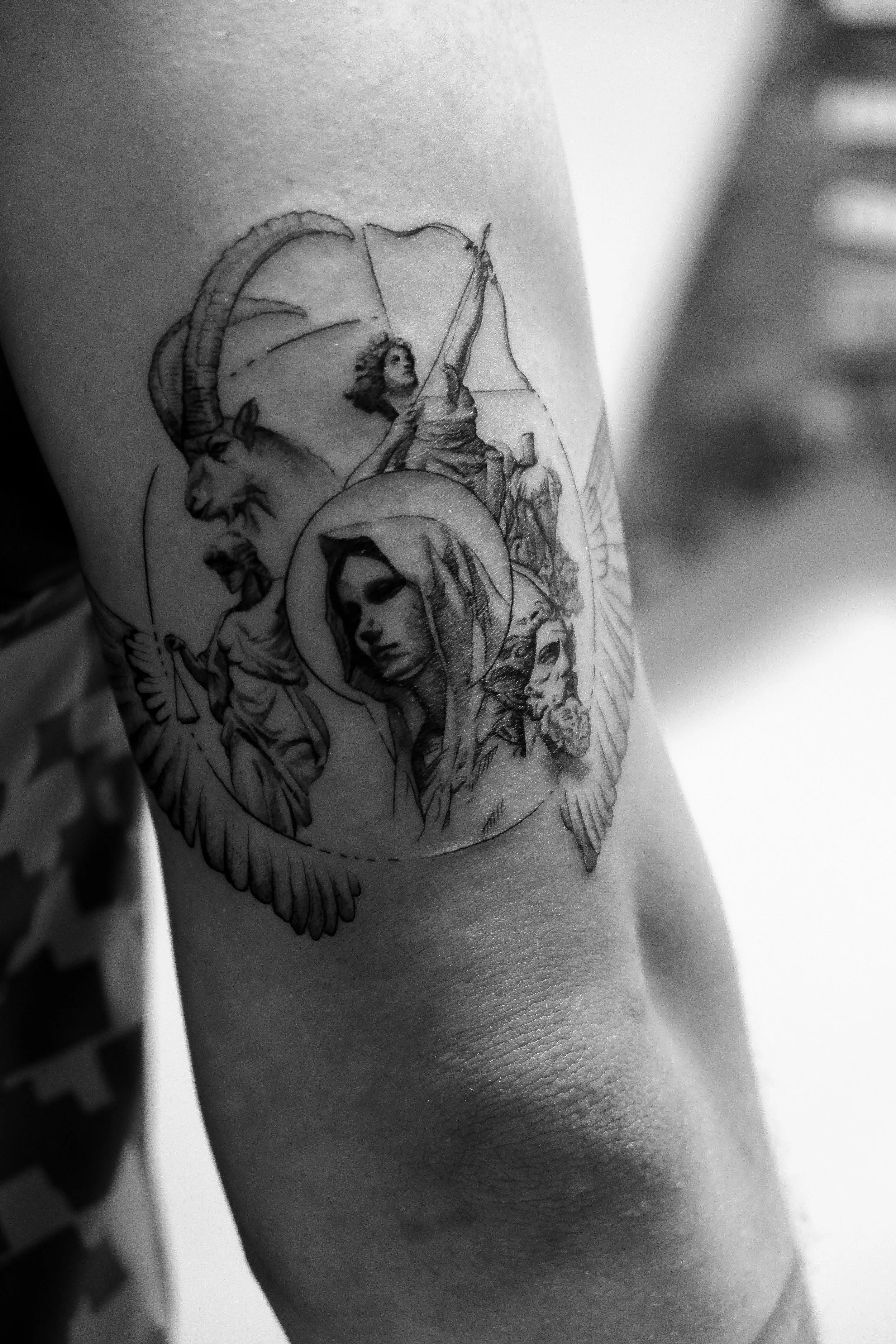 Schwarz-weiß-Tattoo auf dem Oberarm mit religiösen und mythologischen Motiven, darunter Maria, Himmel, Geist und Angel.