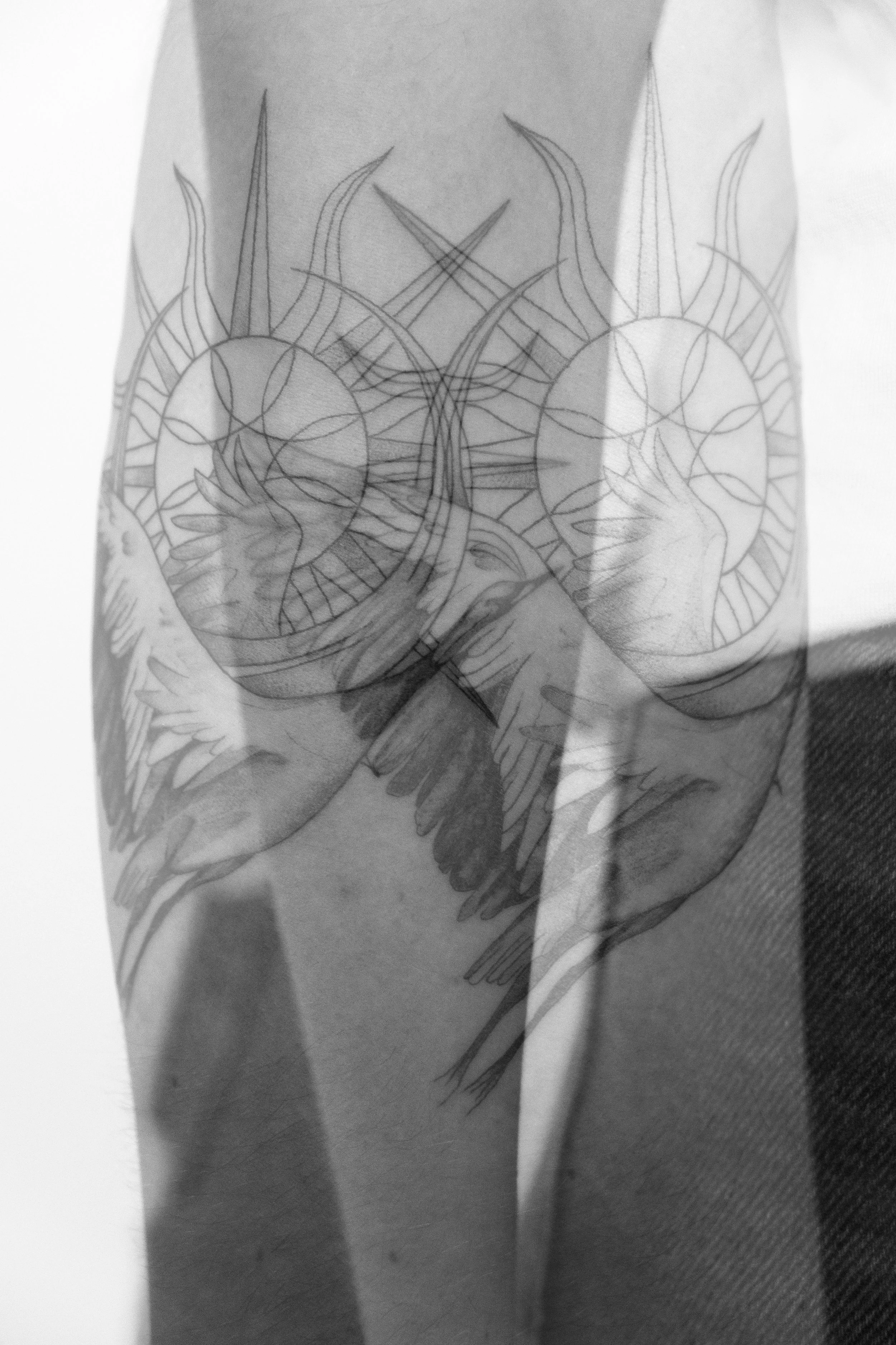 Schwarz-weiße Tattoo-zeichnung von zwei Hufeisen mit Flügeln und Sonnensymbolen in der Mitte, auf einem Arm tätowiert.