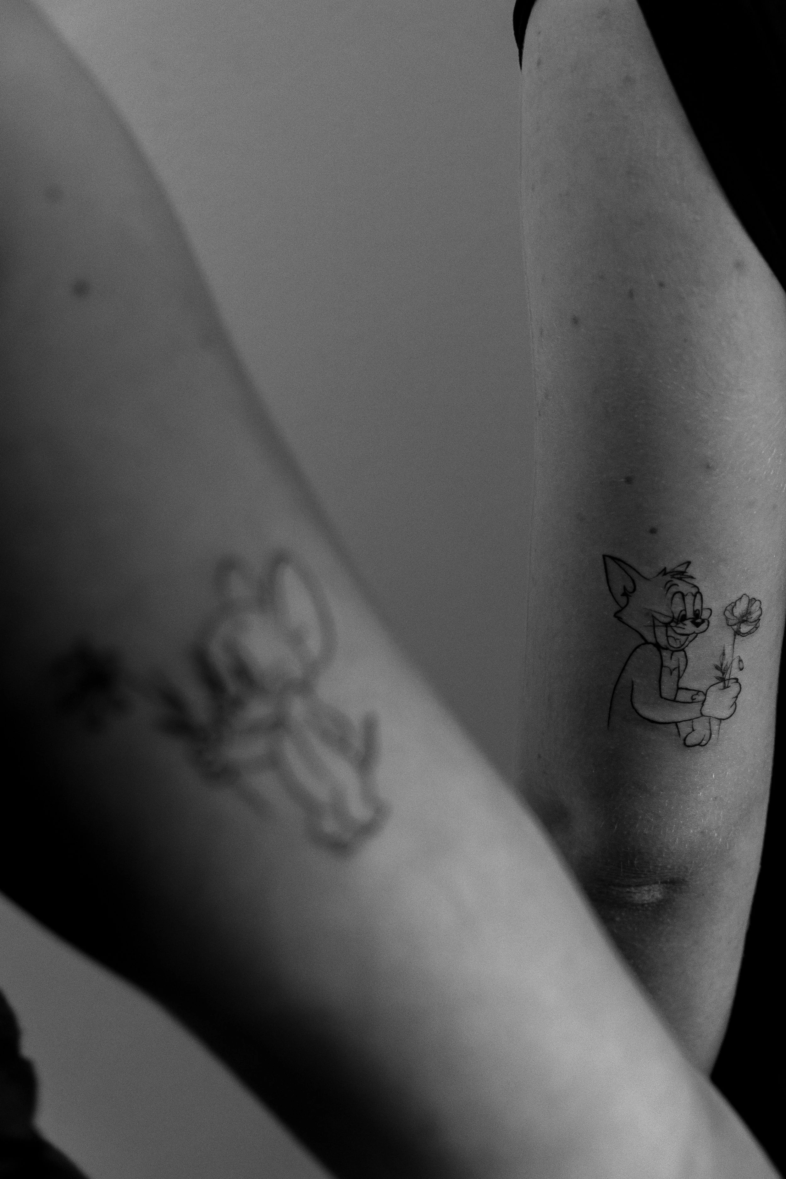 Schwarz-weiß-Tattoo eines Katzencharakters, der eine Blume hält.