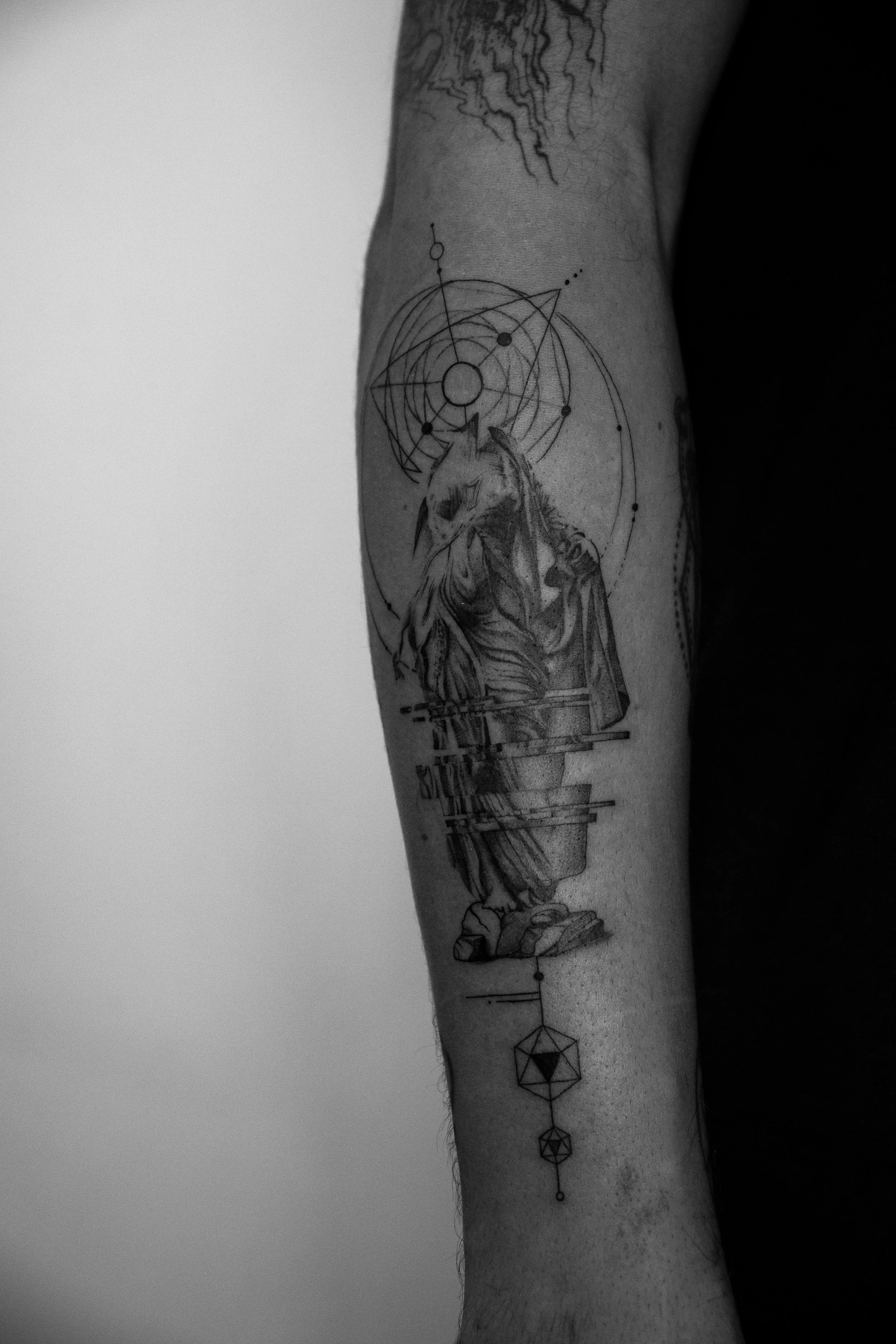 Schwarze Tätowierung eines geometrischen und mystischen Designs, das einen nackten weiblichen Körper und einen Vogel mit einem Menschenkopf zeigt, umgeben von geometrischen Formen und Linien.