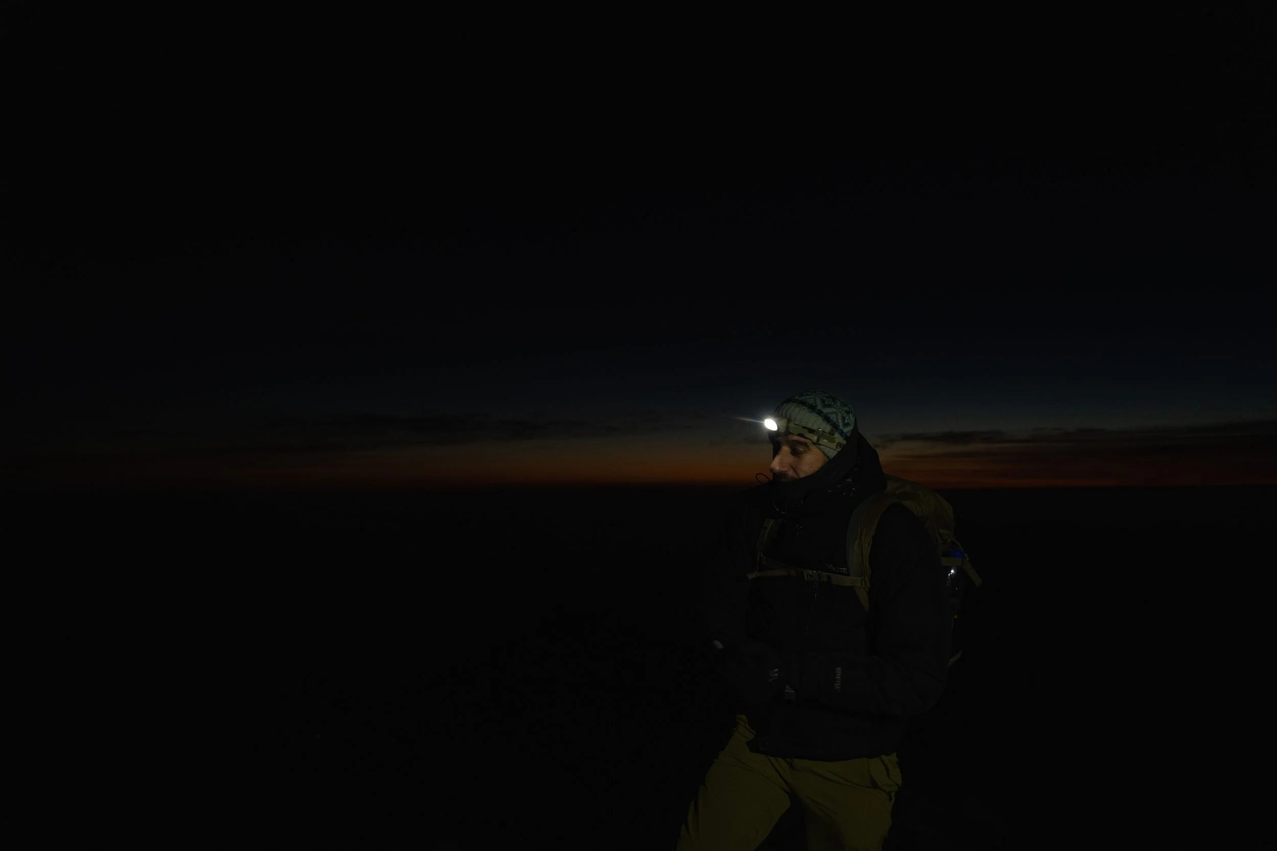 Person wearing a headlamp and outdoor gear running outdoors at dusk or dawn.