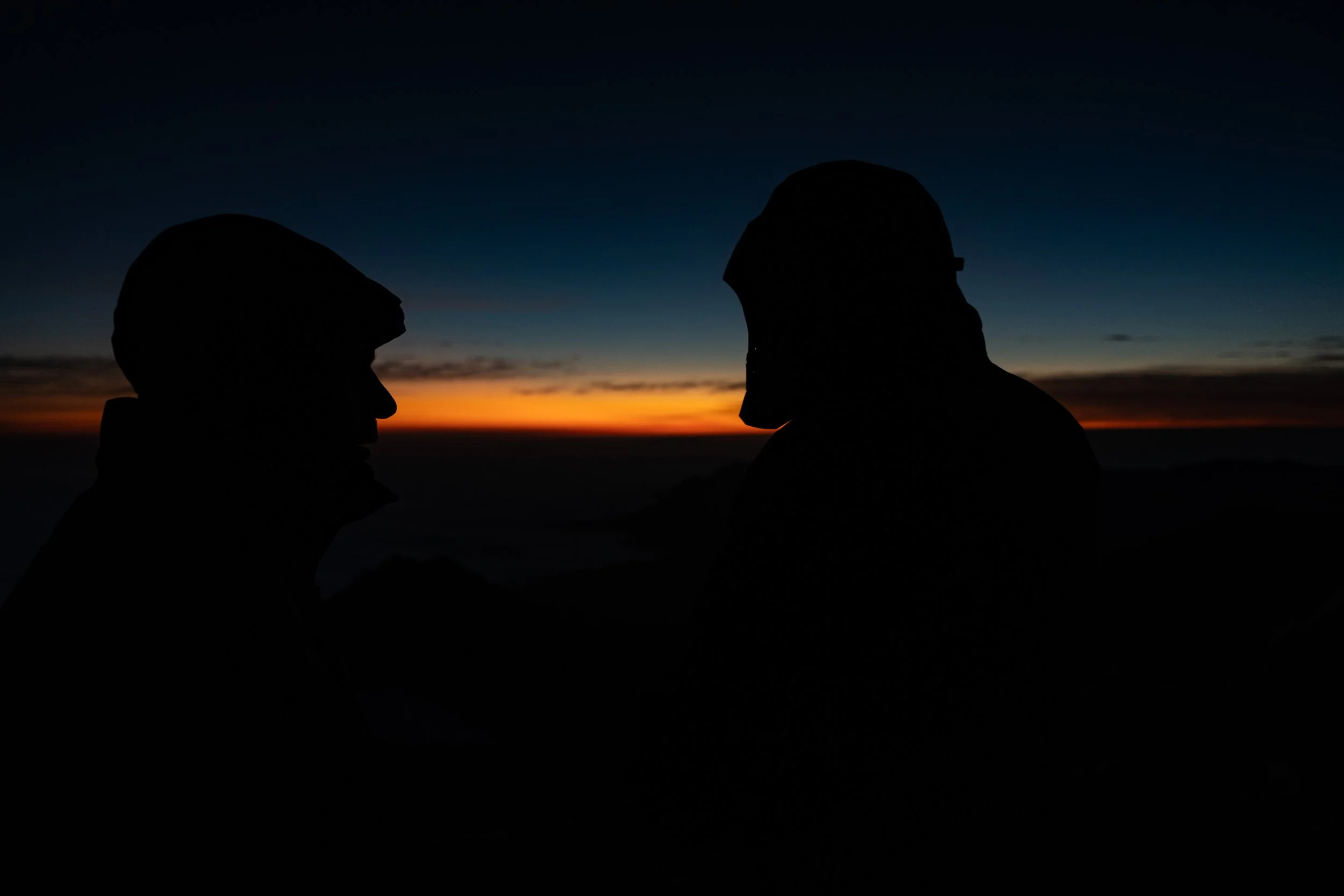 Silhouettes of two people facing each other against a colorful sunset sky.