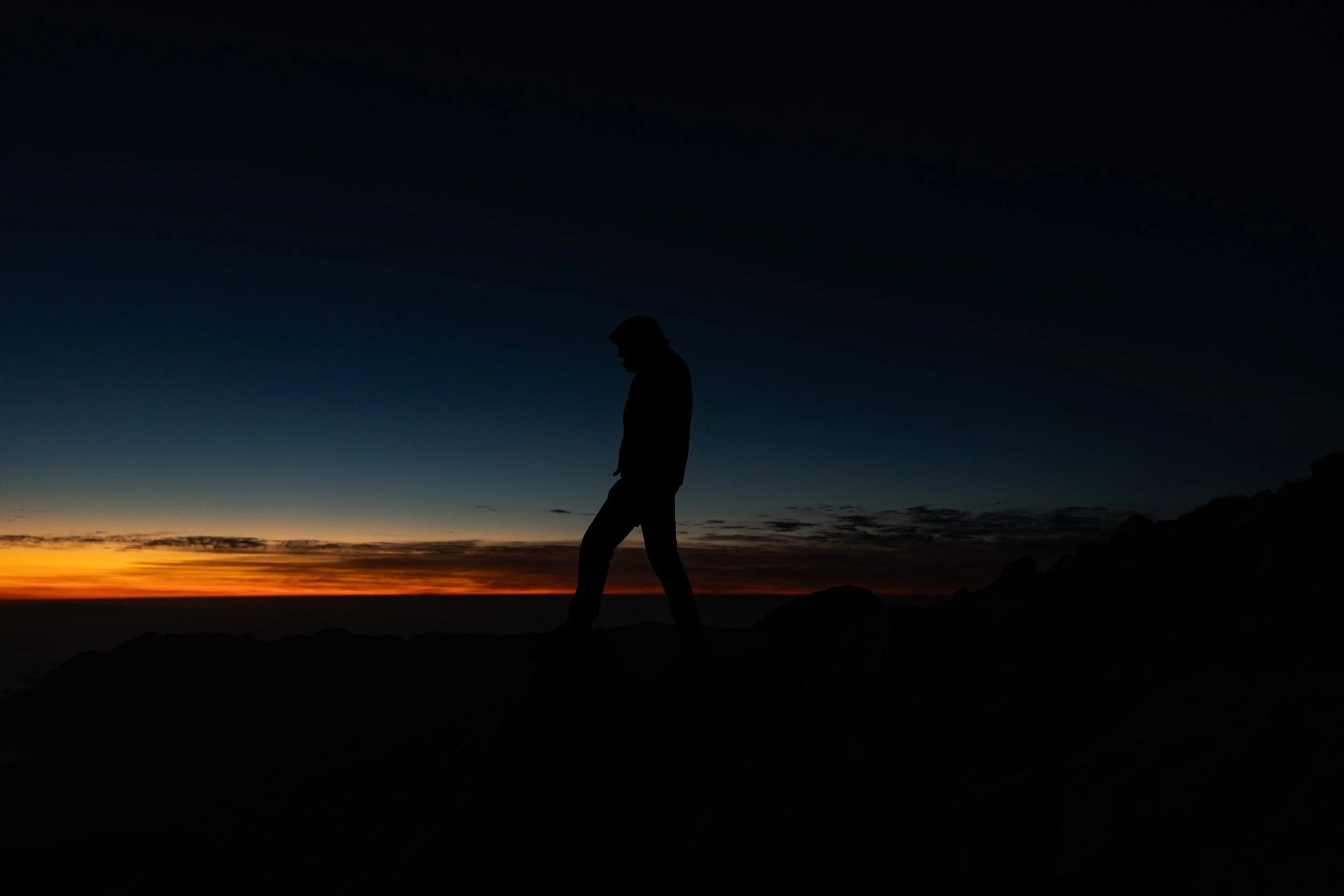 Silhouette of a person standing on rocks during sunset or twilight with a darkening sky and distant horizon