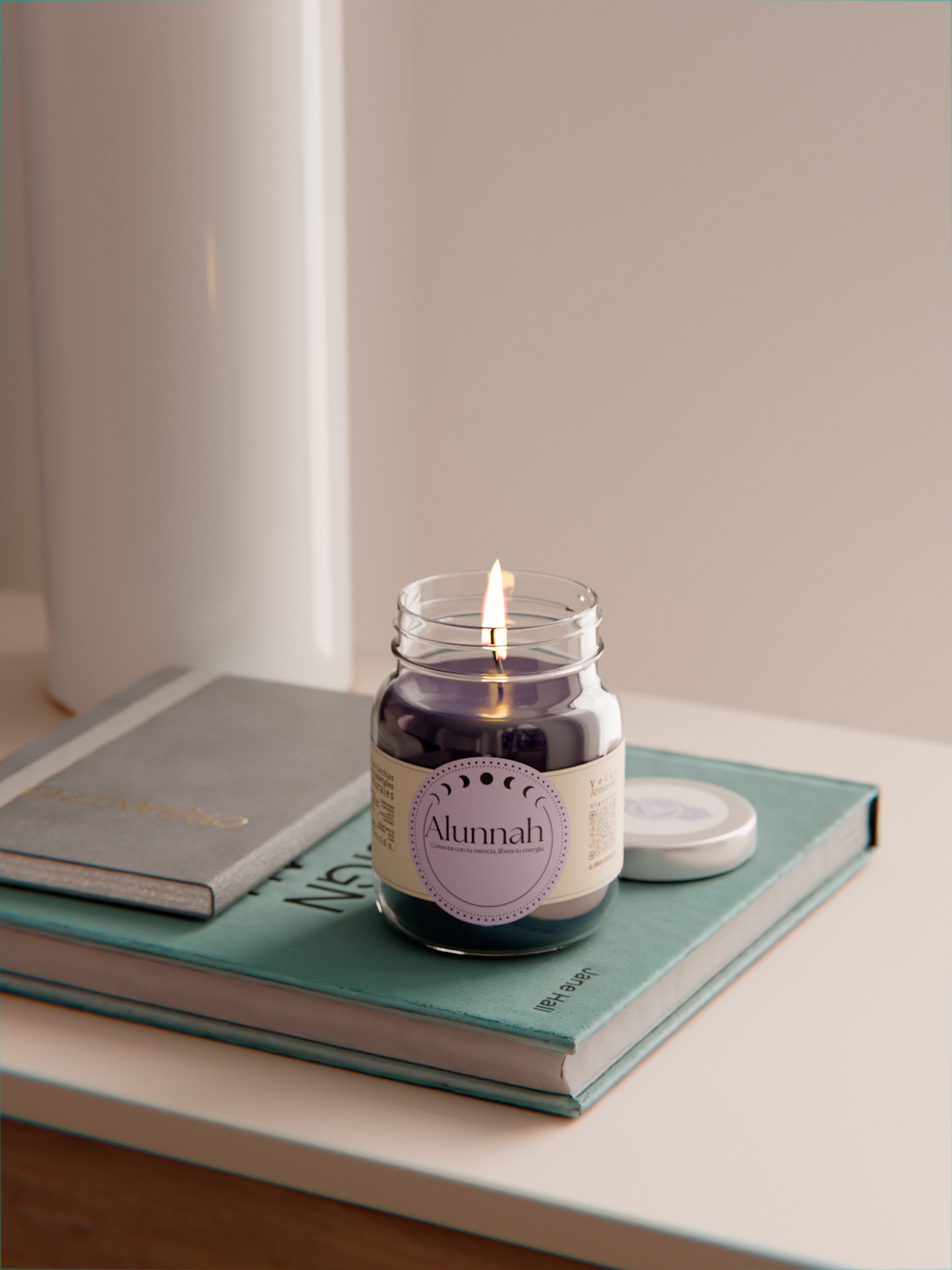 A lit black candle in a glass jar labeled 'Alunnah' resting on a stack of two books, on a beige surface with a blurred white wall in the background.