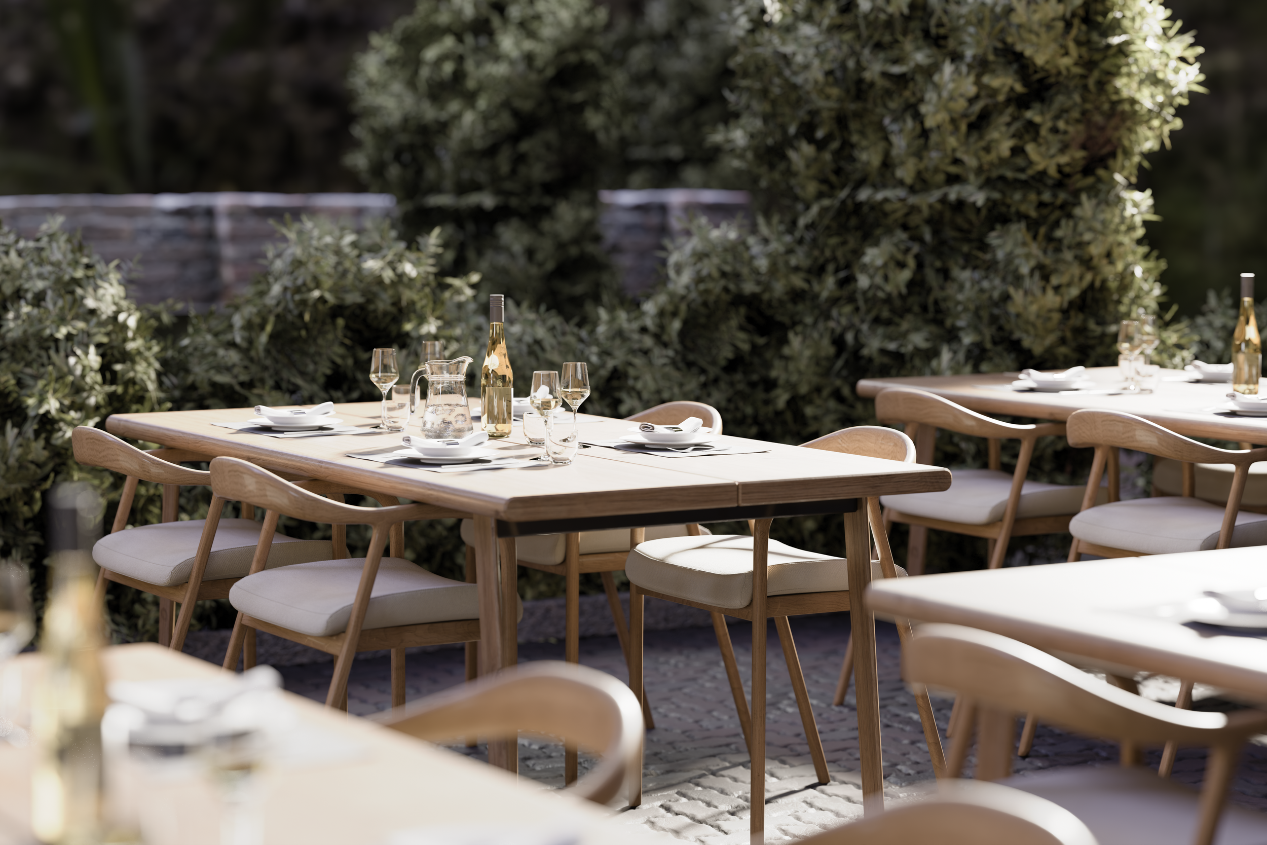 Outdoor dining area with wooden tables, chairs, wine bottles, glasses, and place settings, surrounded by greenery.