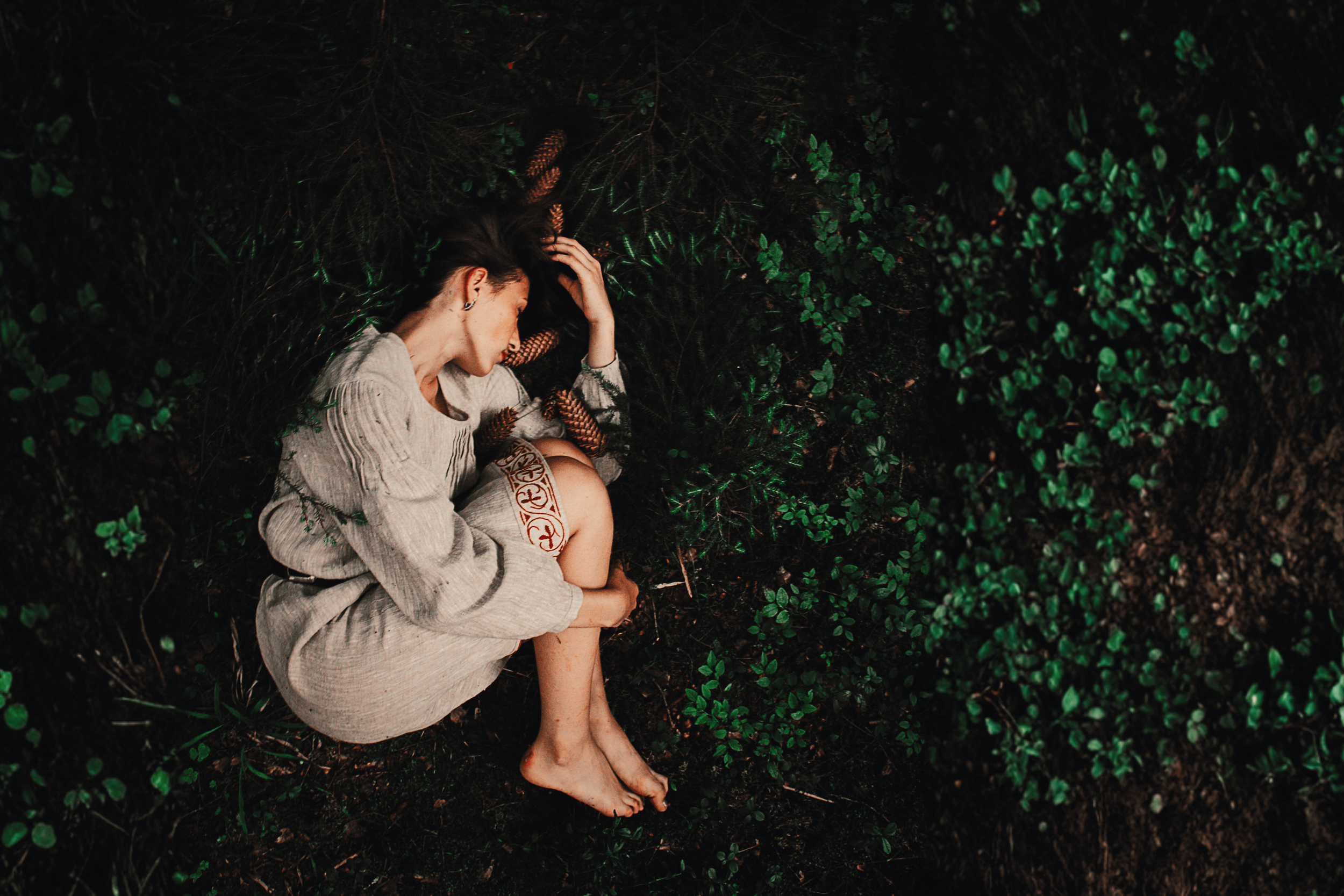 Person curled in leaves symbolizing somatic healing, safety, and womb-like emotional support.