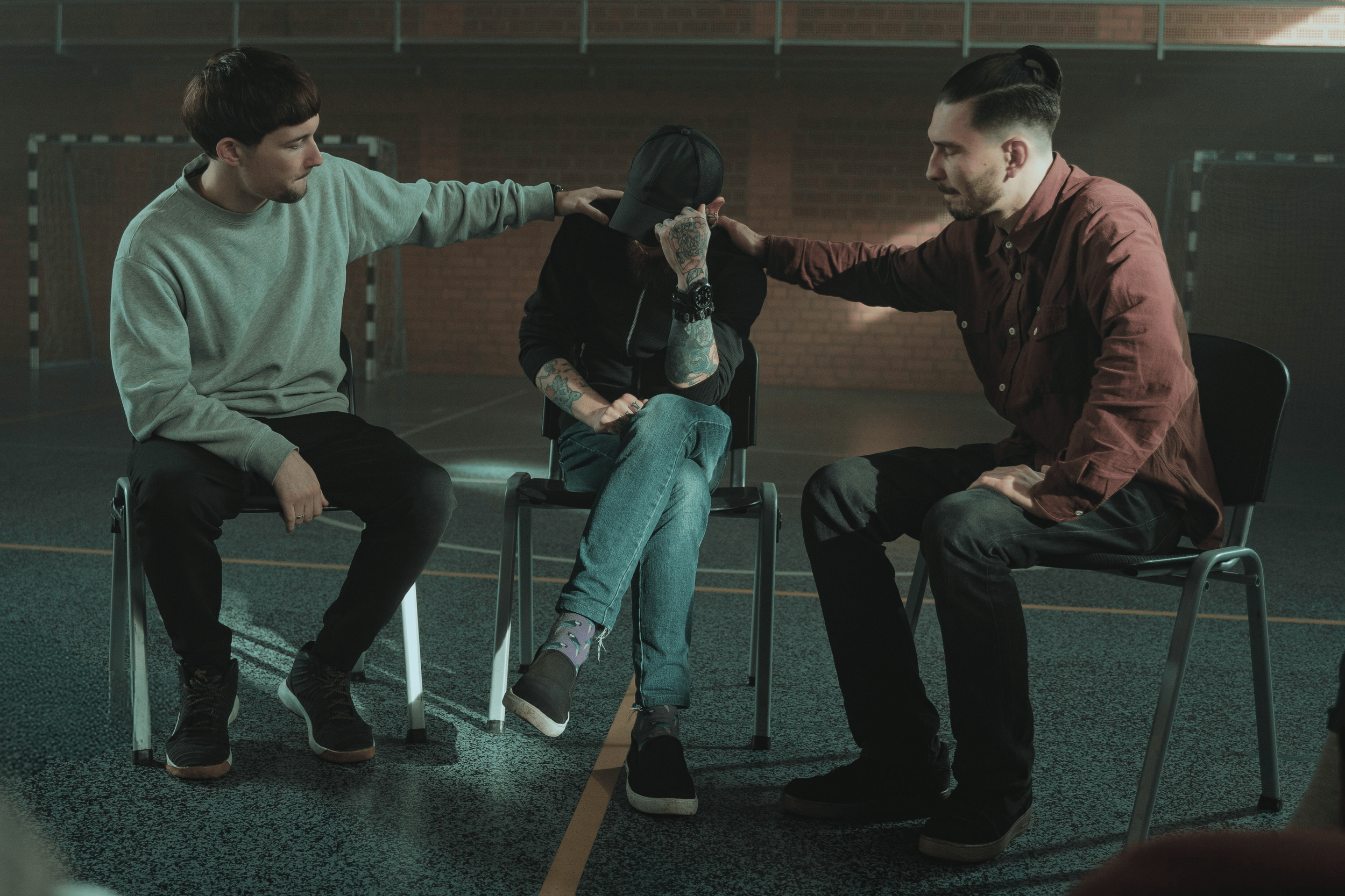 Group of men in a supportive space, with two holding the shoulders of the man in the middle, symbolizing emotional safety and attuned self-leadership