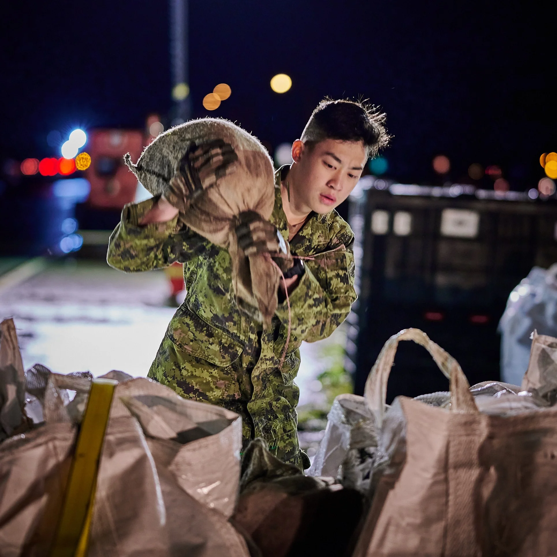 A soldier in camouflage uniform holding a large seashell at night, with blurred city lights in the background.