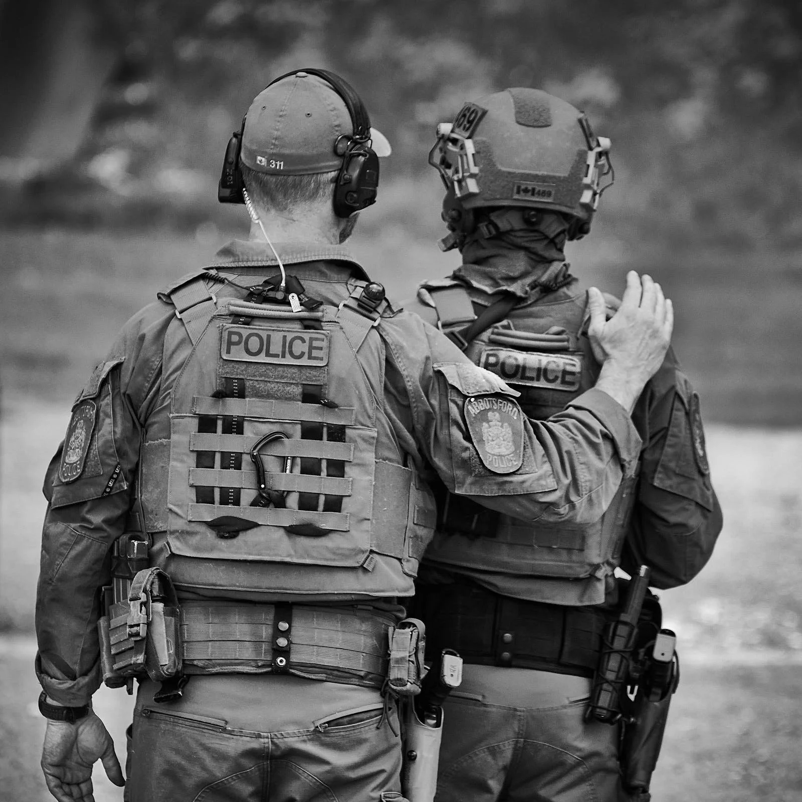 Two police officers, seen from the back, engaged in a conversation outdoors. One officer has an arm around the other's shoulder.