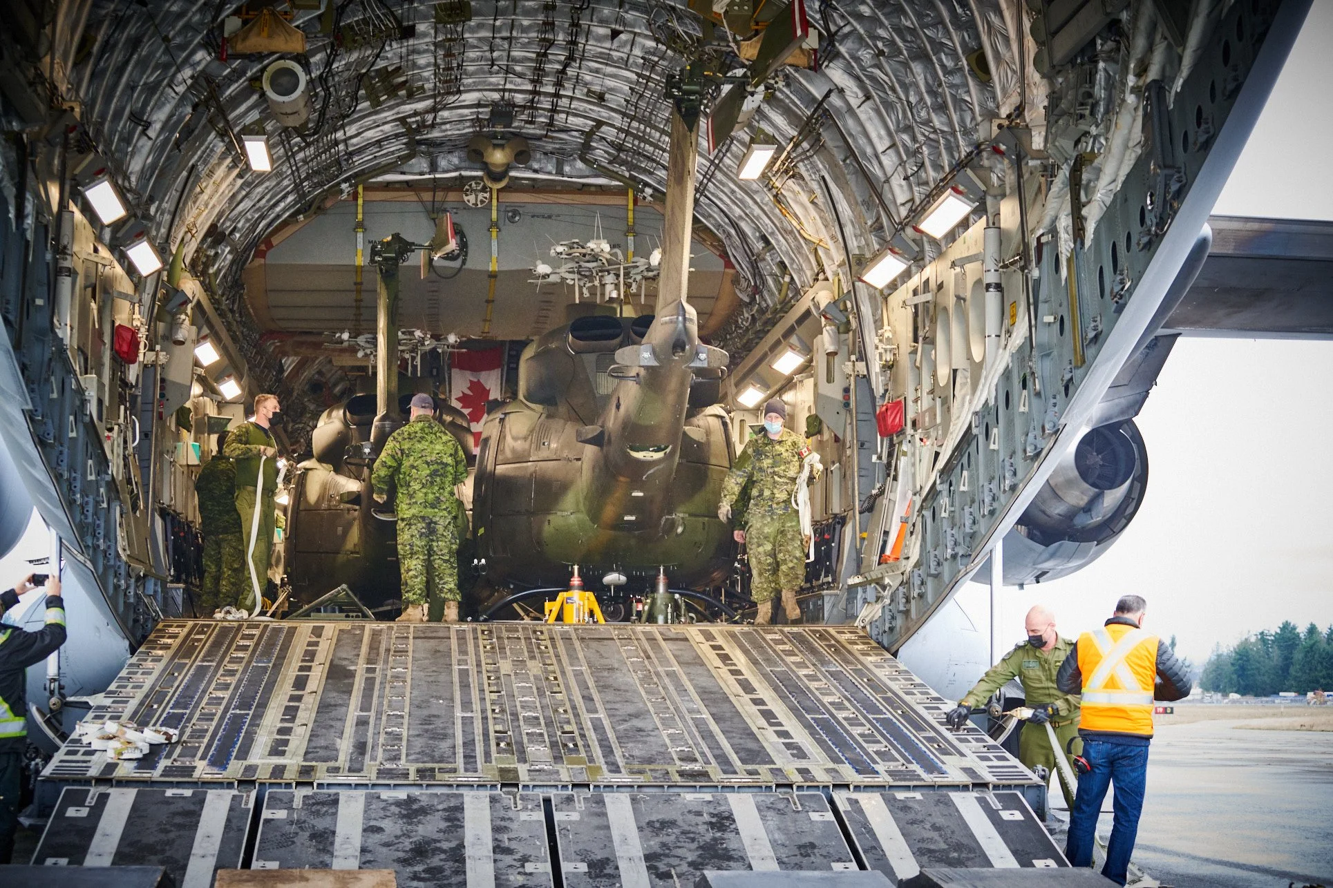 Military personnel loading a helicopter with supplies through the rear ramp of a large cargo aircraft.