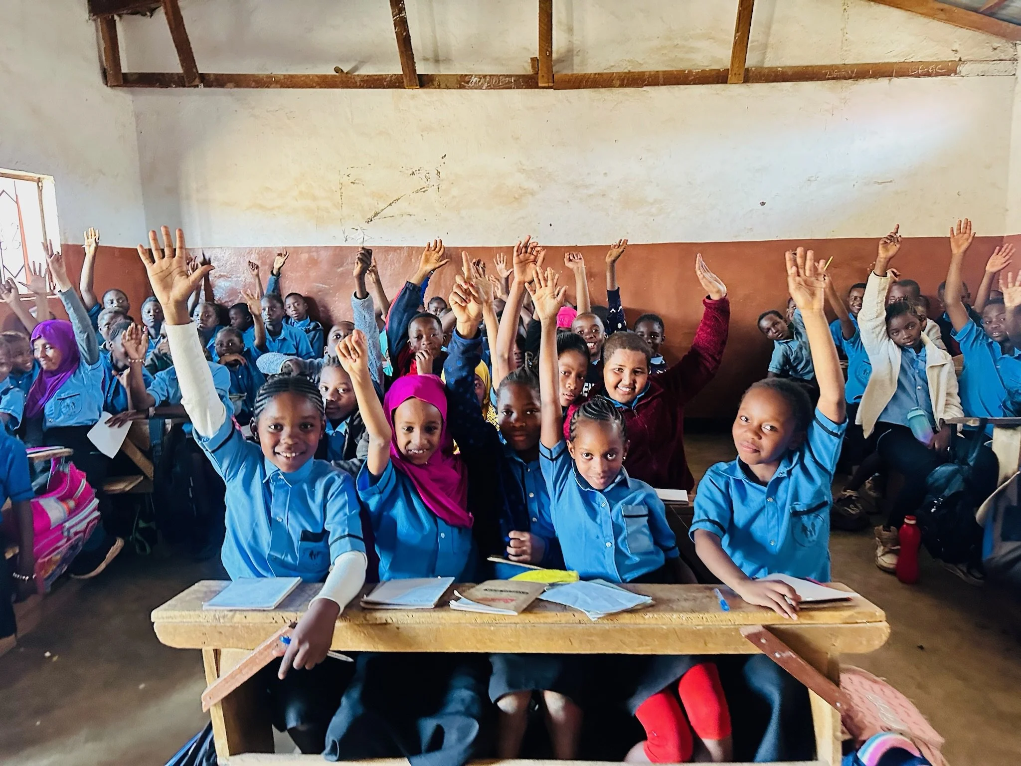 a classroom of students in malawi all raising their hands