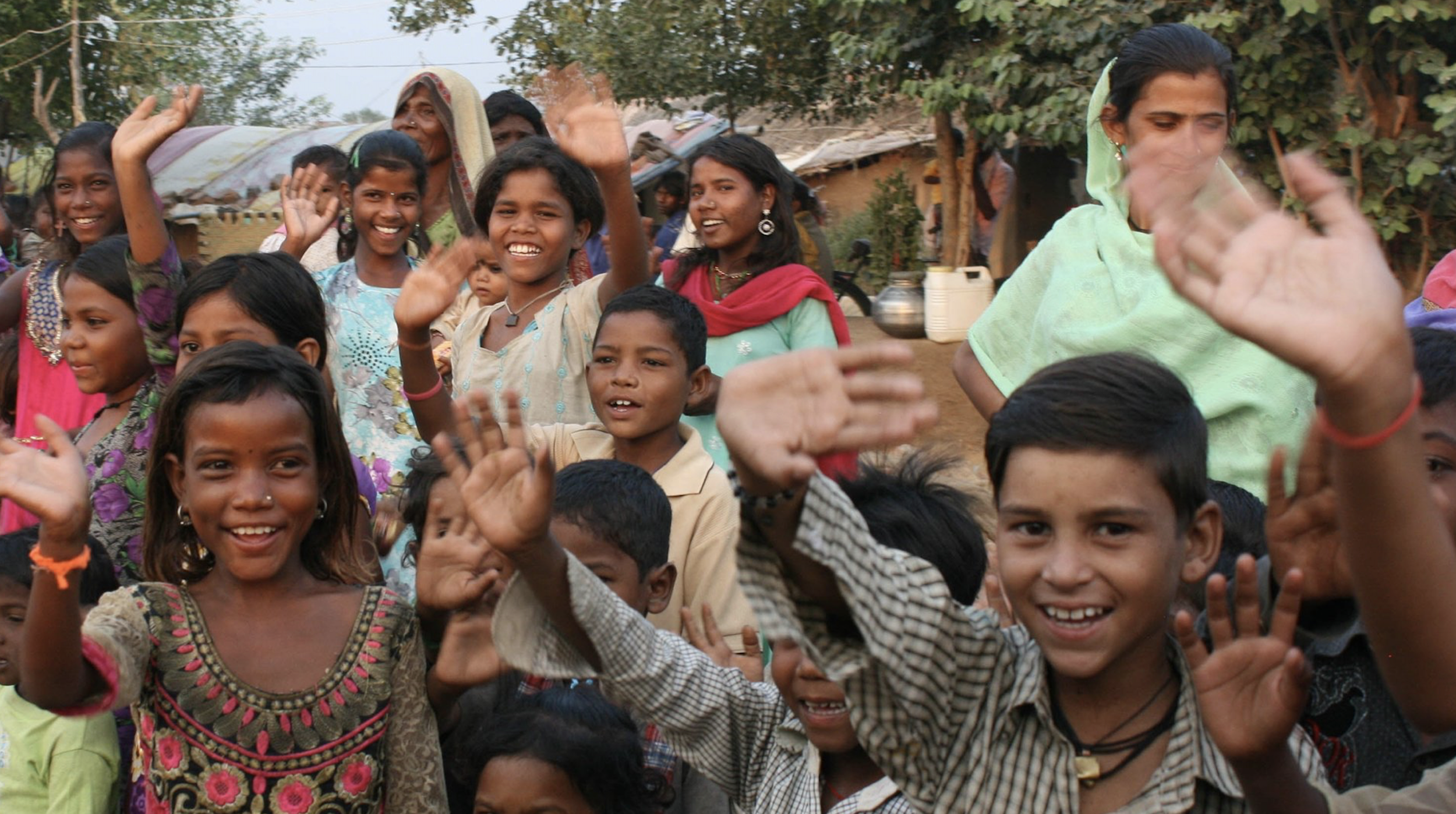 a large group of school kids in india smiling and waving at the camera