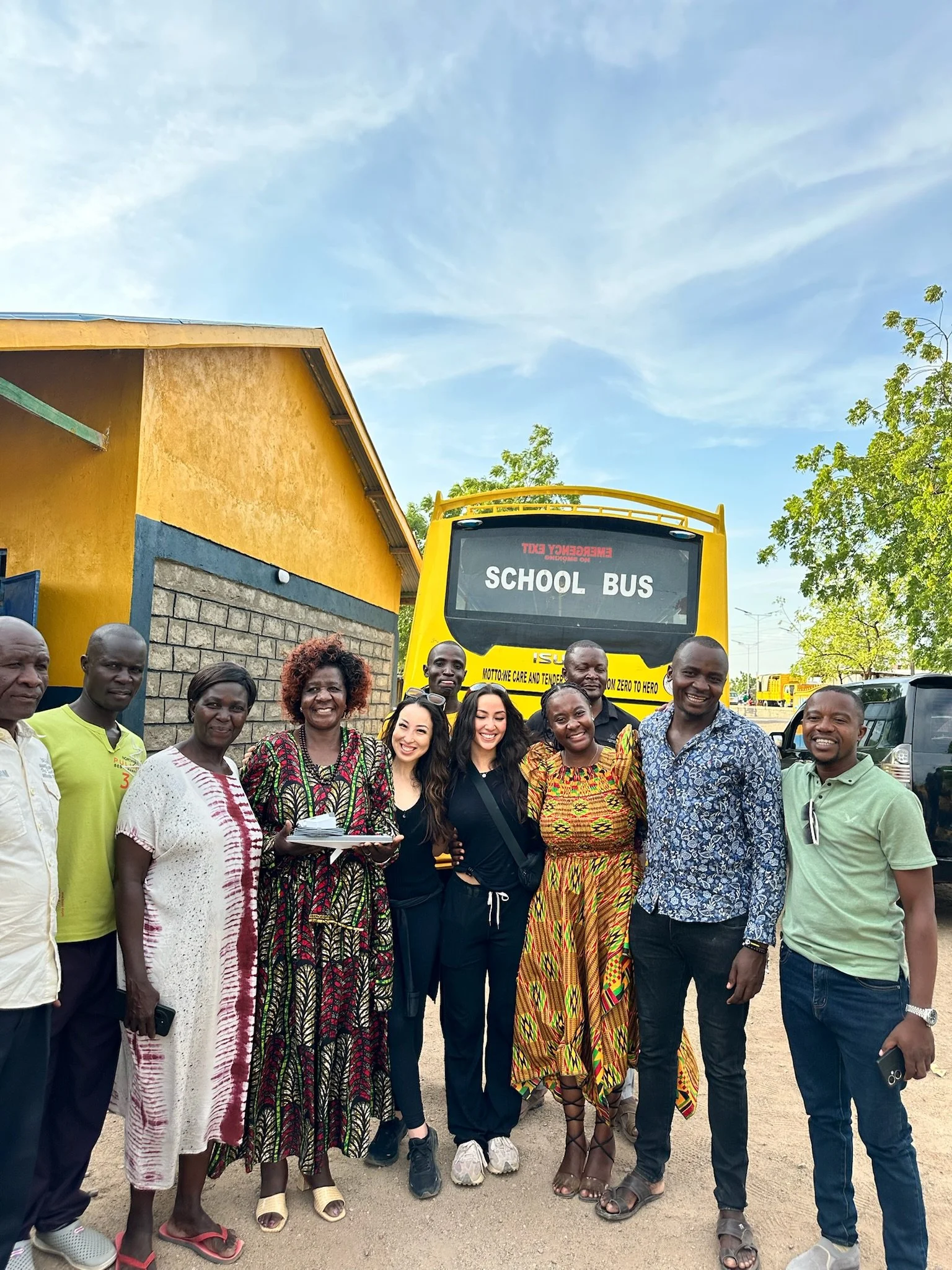 a group of school teachers in africa smiling as they stand in front of a school bus