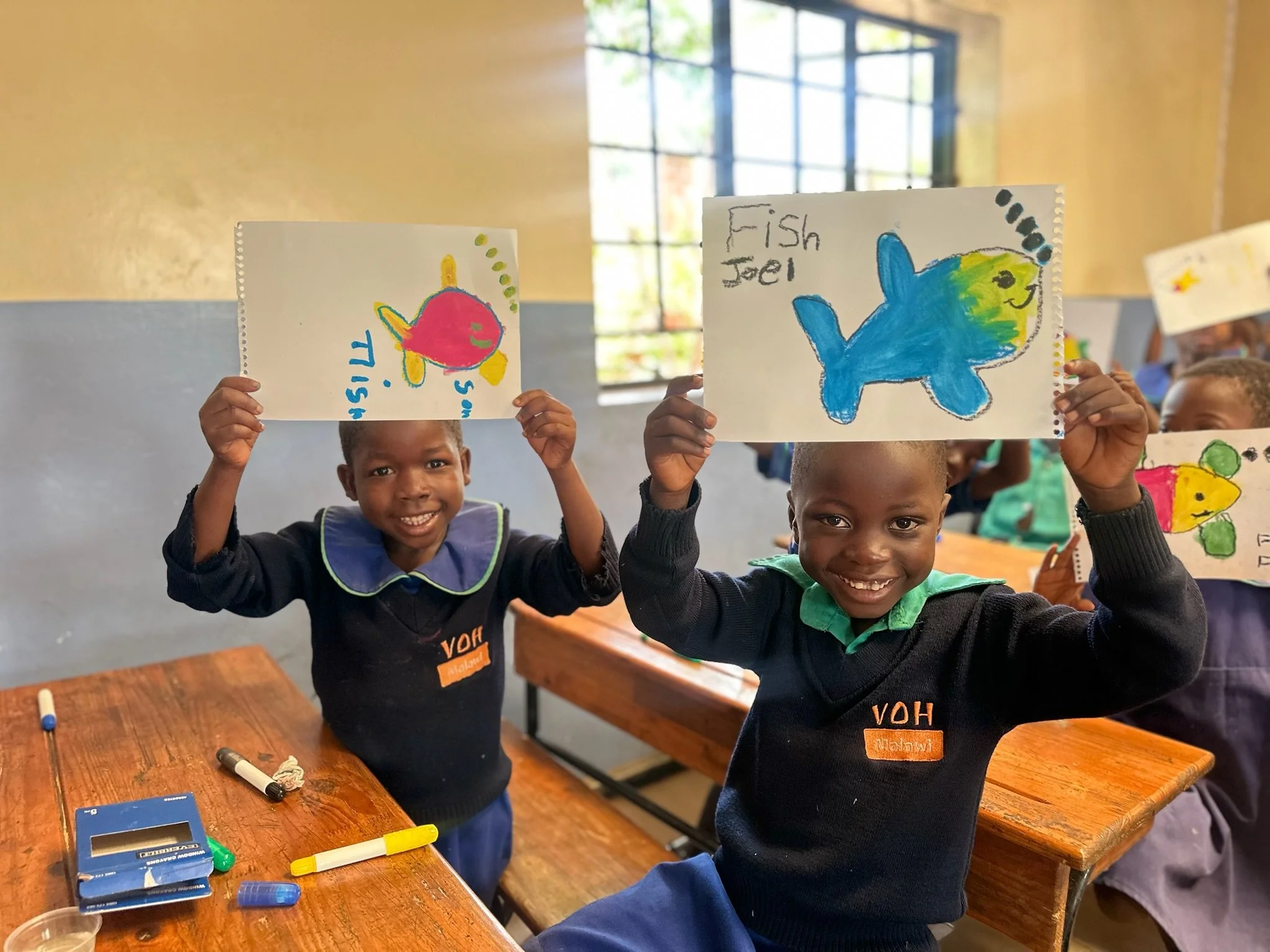 two young school children in malawi smiling and holding their drawings above their heads