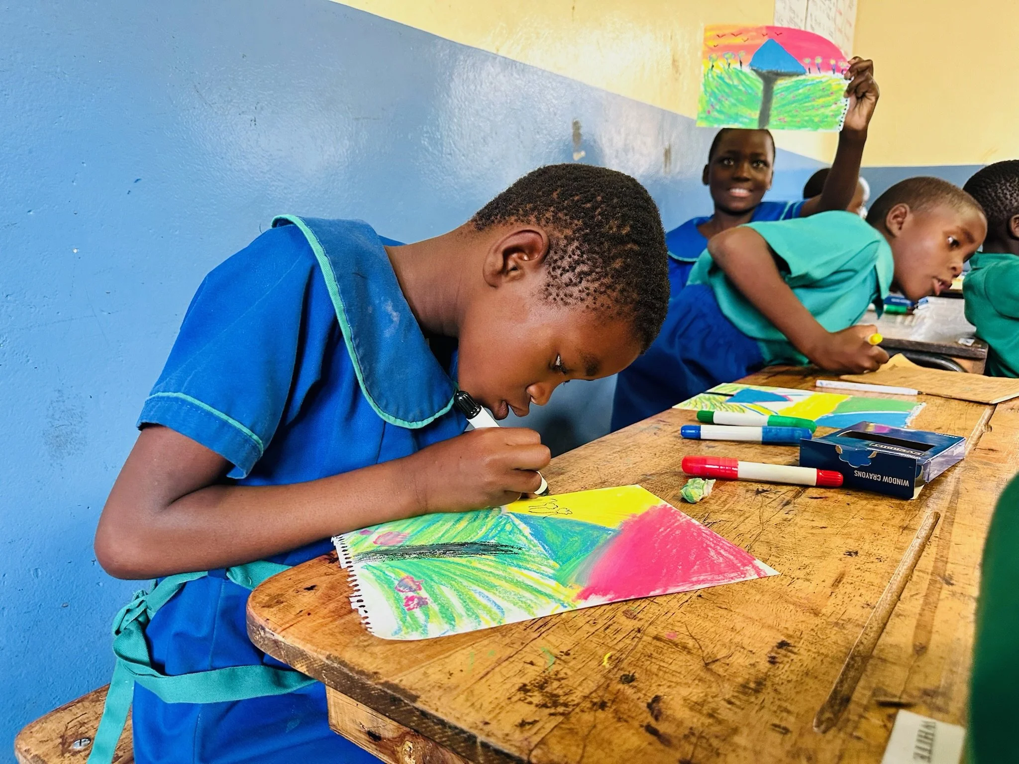 a school girl in malawi sitting at a desk and painting a picture