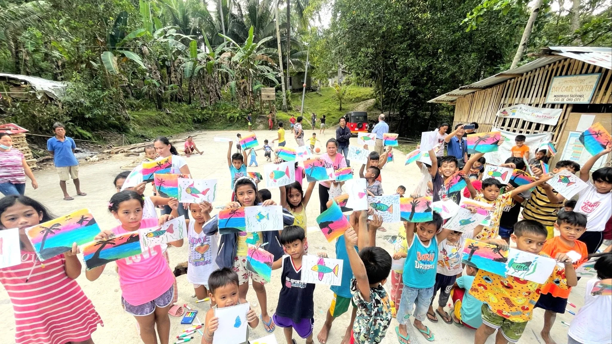 a group of kids in the philippines outside holding up their artwork