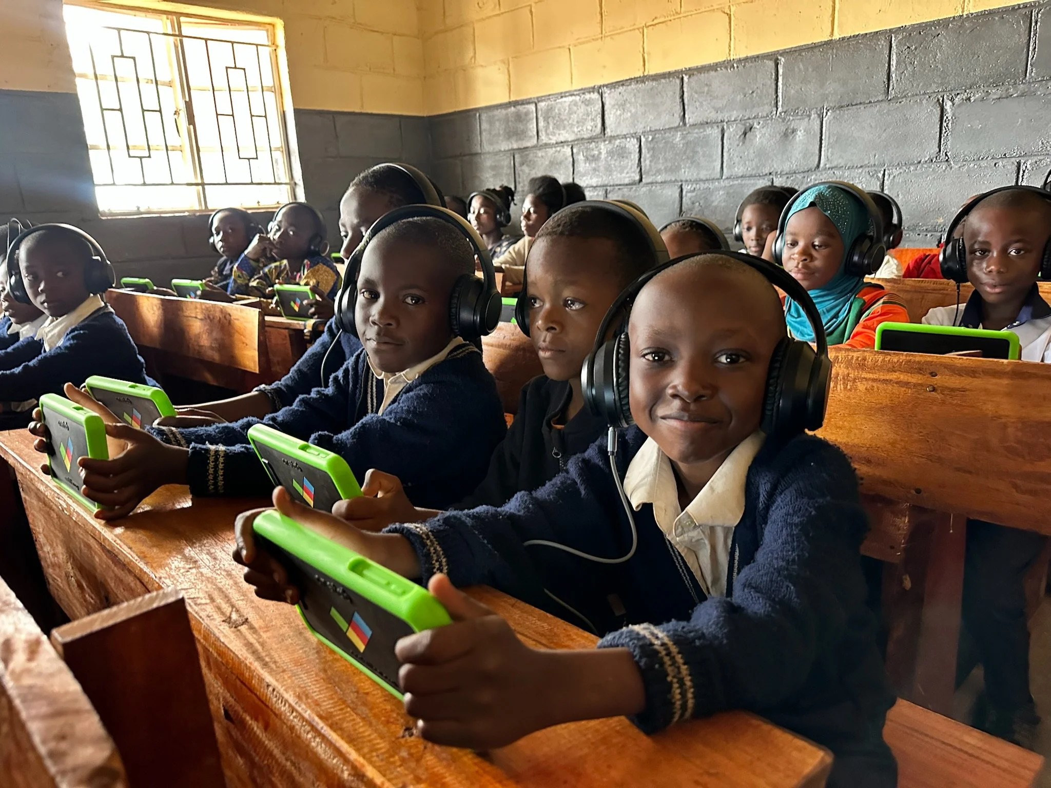school kids in malawi in a classroom with headphones on using learning tablets