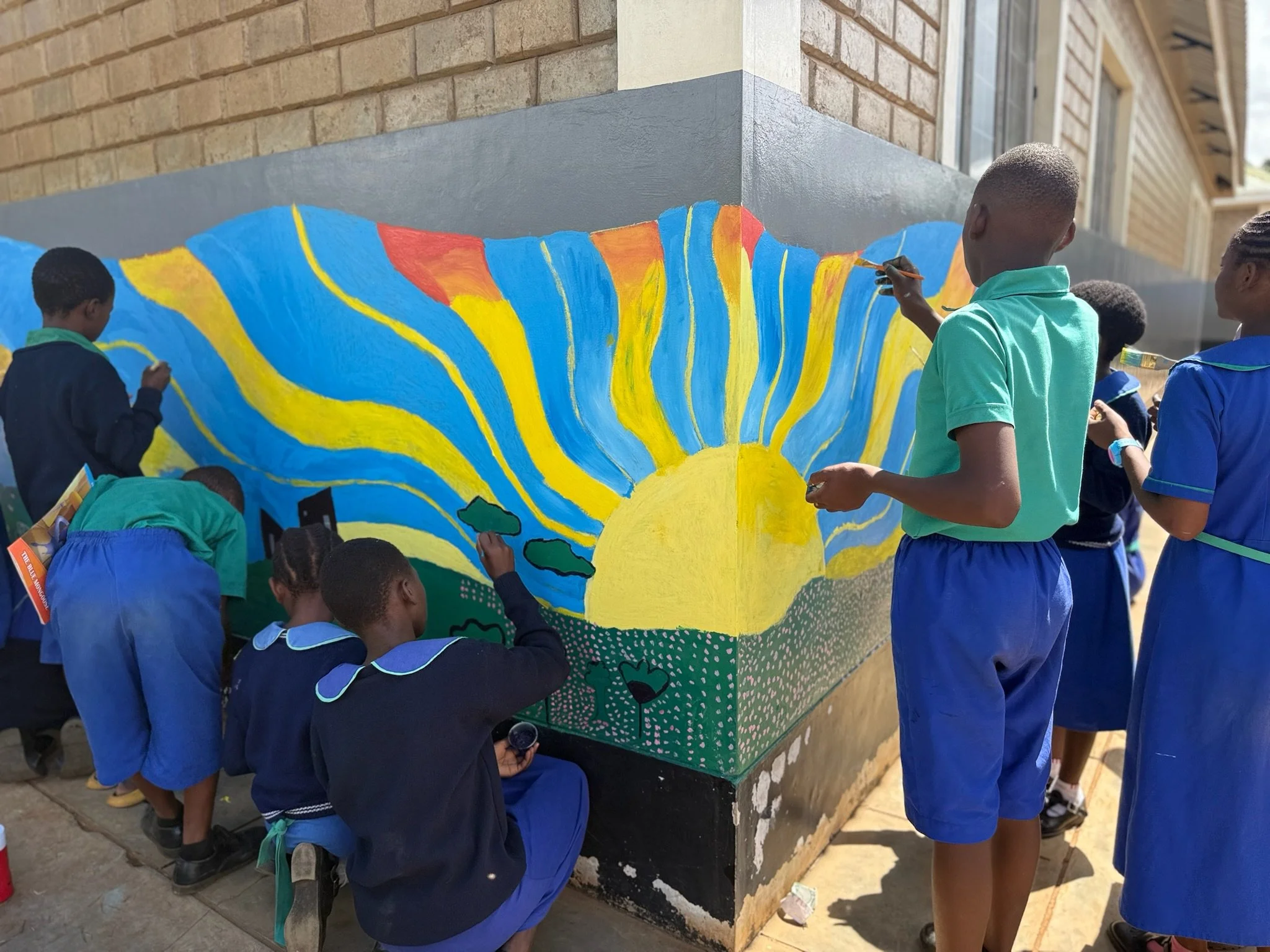 kids in malawi painting a mural of a sun on a wall