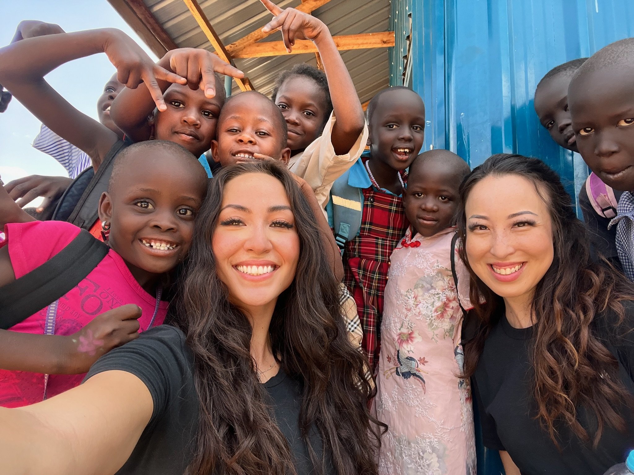image of a group of kenyan school children smiling at the camera with 2 volunteers