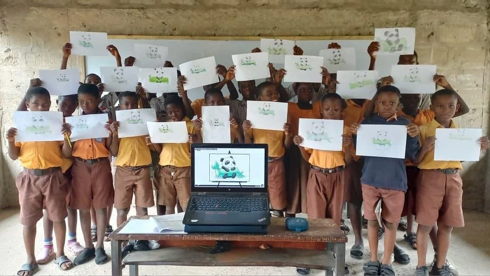 image of a class of ghanan students holding up their artwork and smiling at the camera