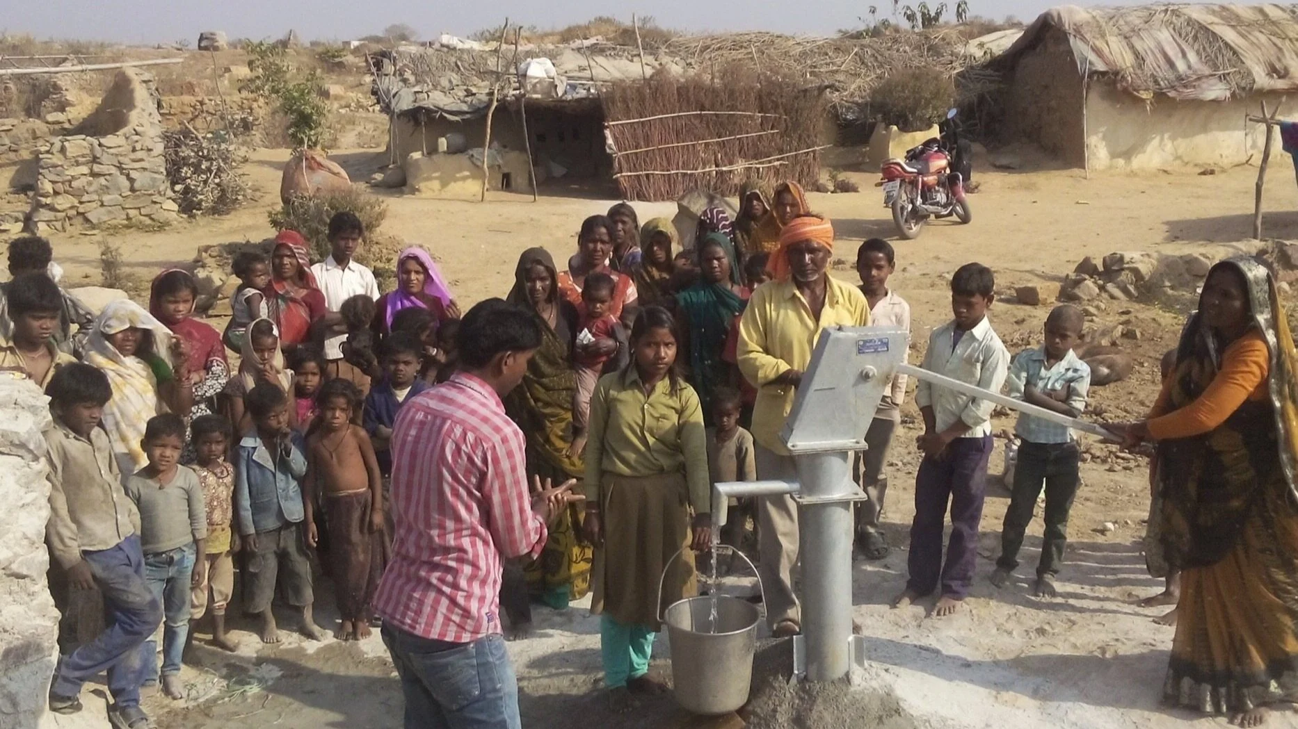 a large group of people standing outside around a water pump