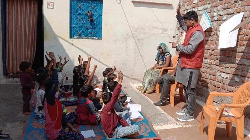 a small group of school kids in india doing class outside with their hands raised in the air