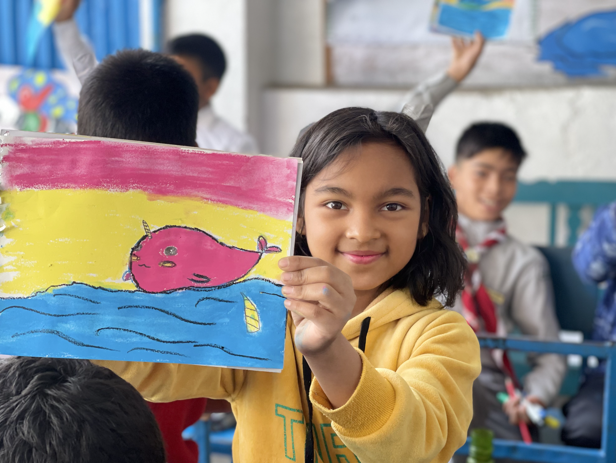 a young girl holding up her painting of a pink narwhal