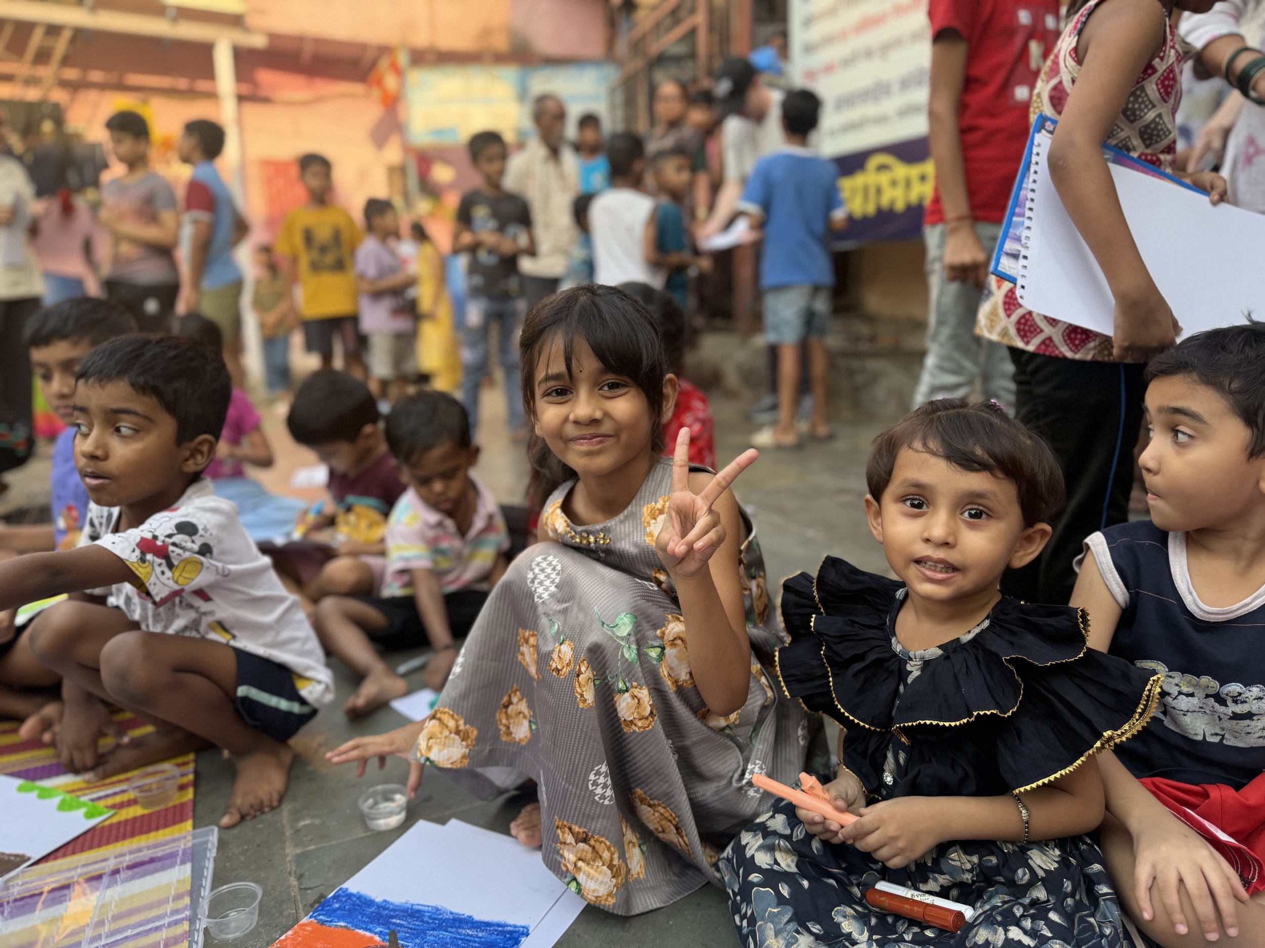 image of a few kids in india sitting on the ground doing art and smiling at the camera