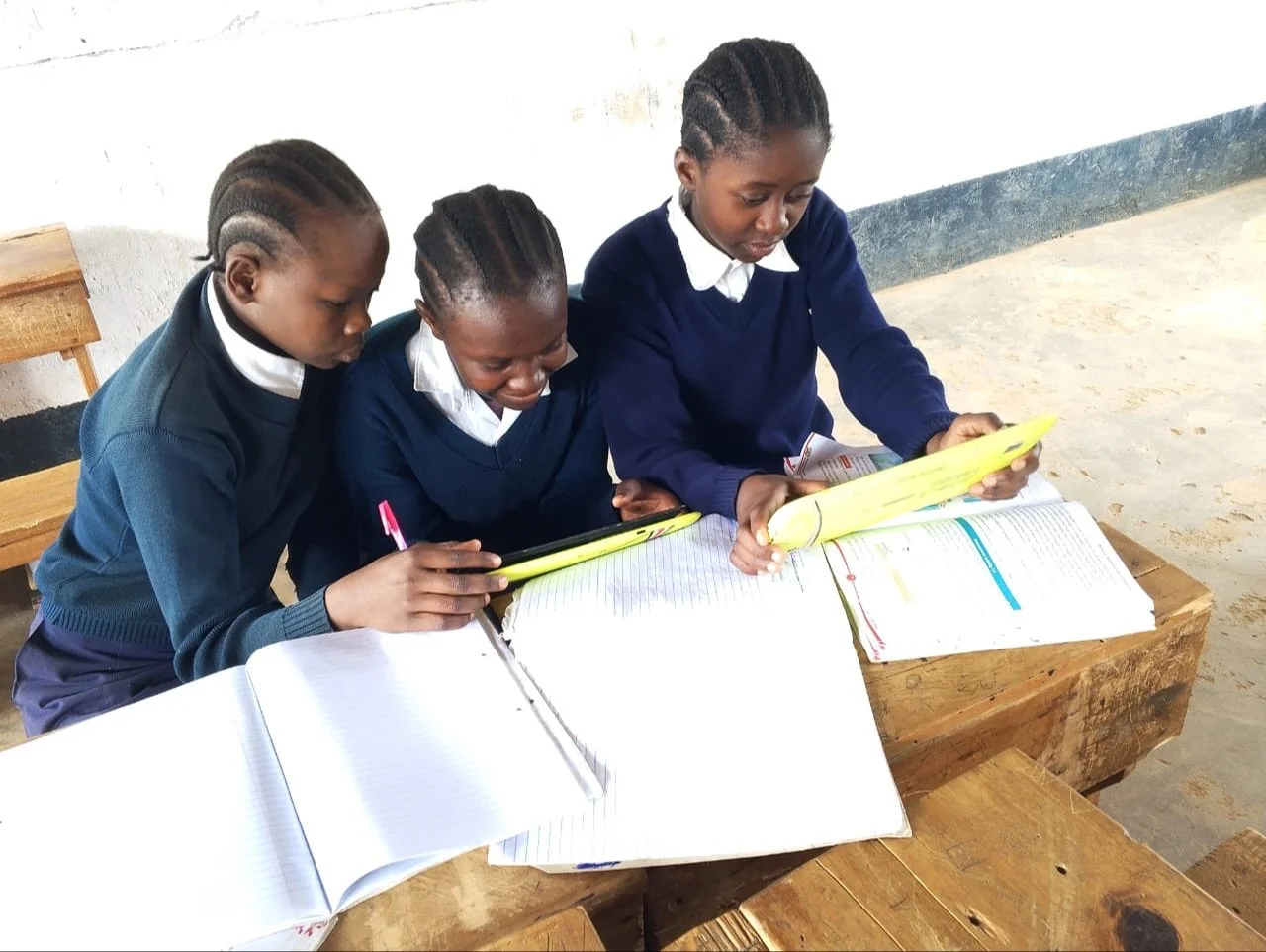 image of 3 school kids in Kenya doing school work and using tablets