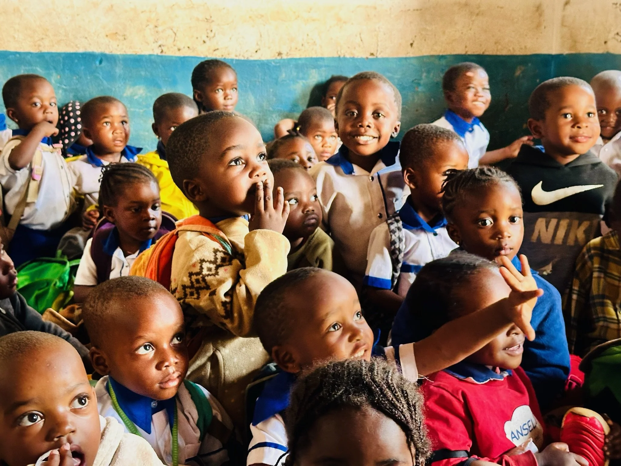 a group of very young school kids sitting on the floor of a classroom