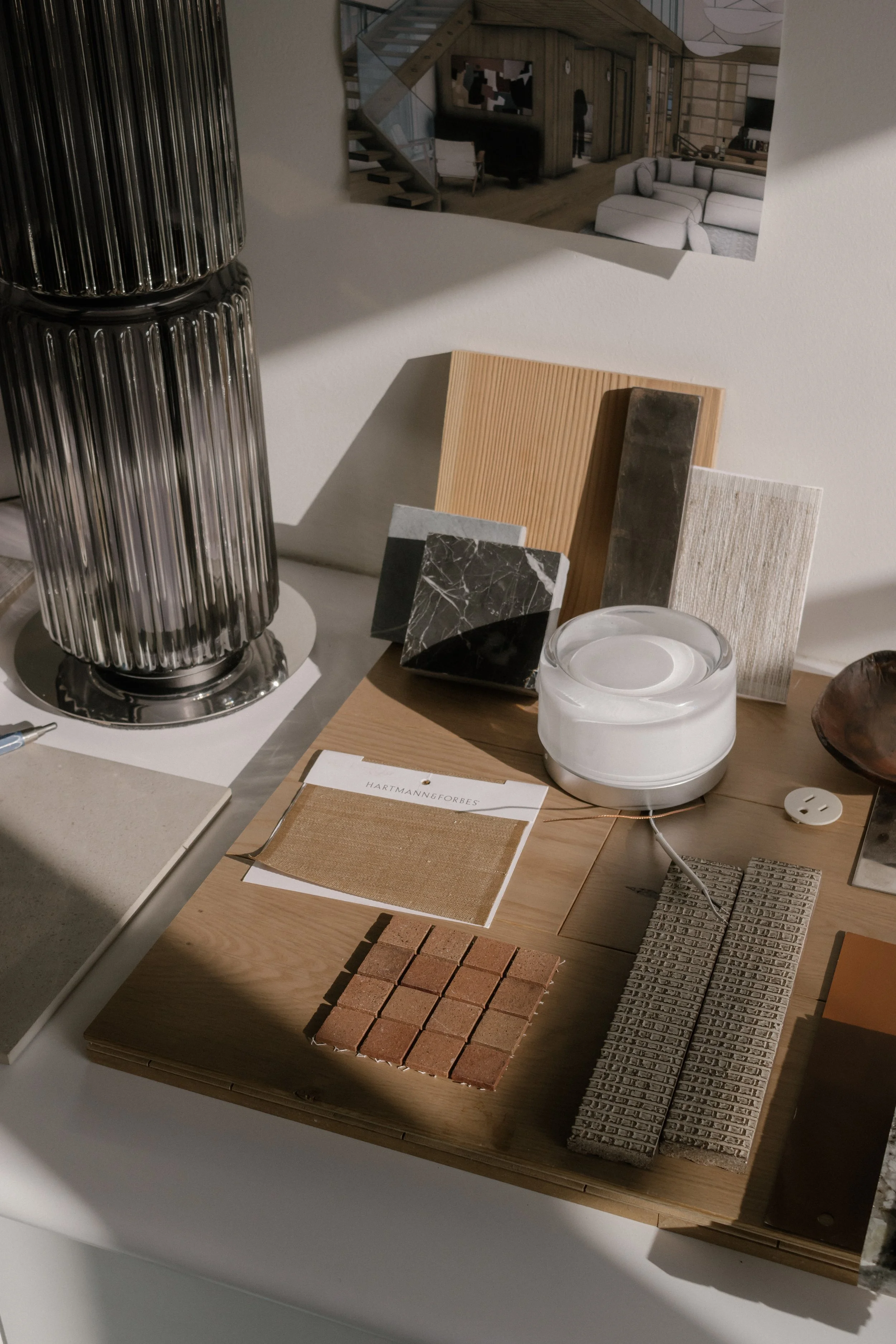 Interior design samples and materials on a wooden table, with a mirror reflecting part of a living room in the background.
