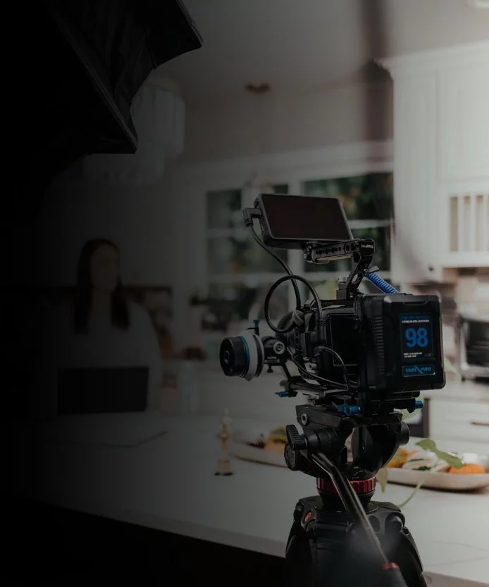 Professional video camera mounted on a tripod filming a woman in a kitchen.