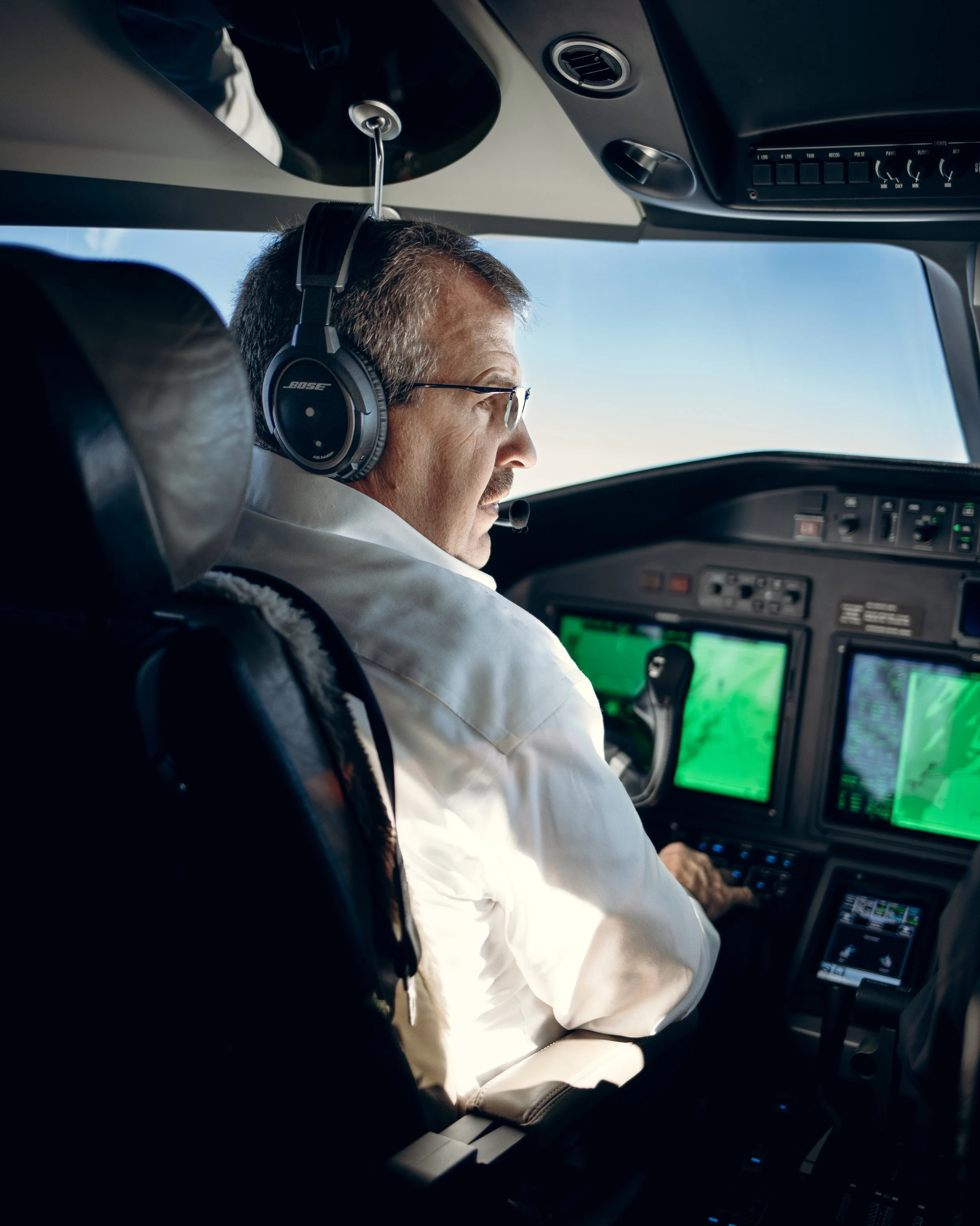 Pilot in cockpit wearing headphones, looking towards the aircraft controls and displays.