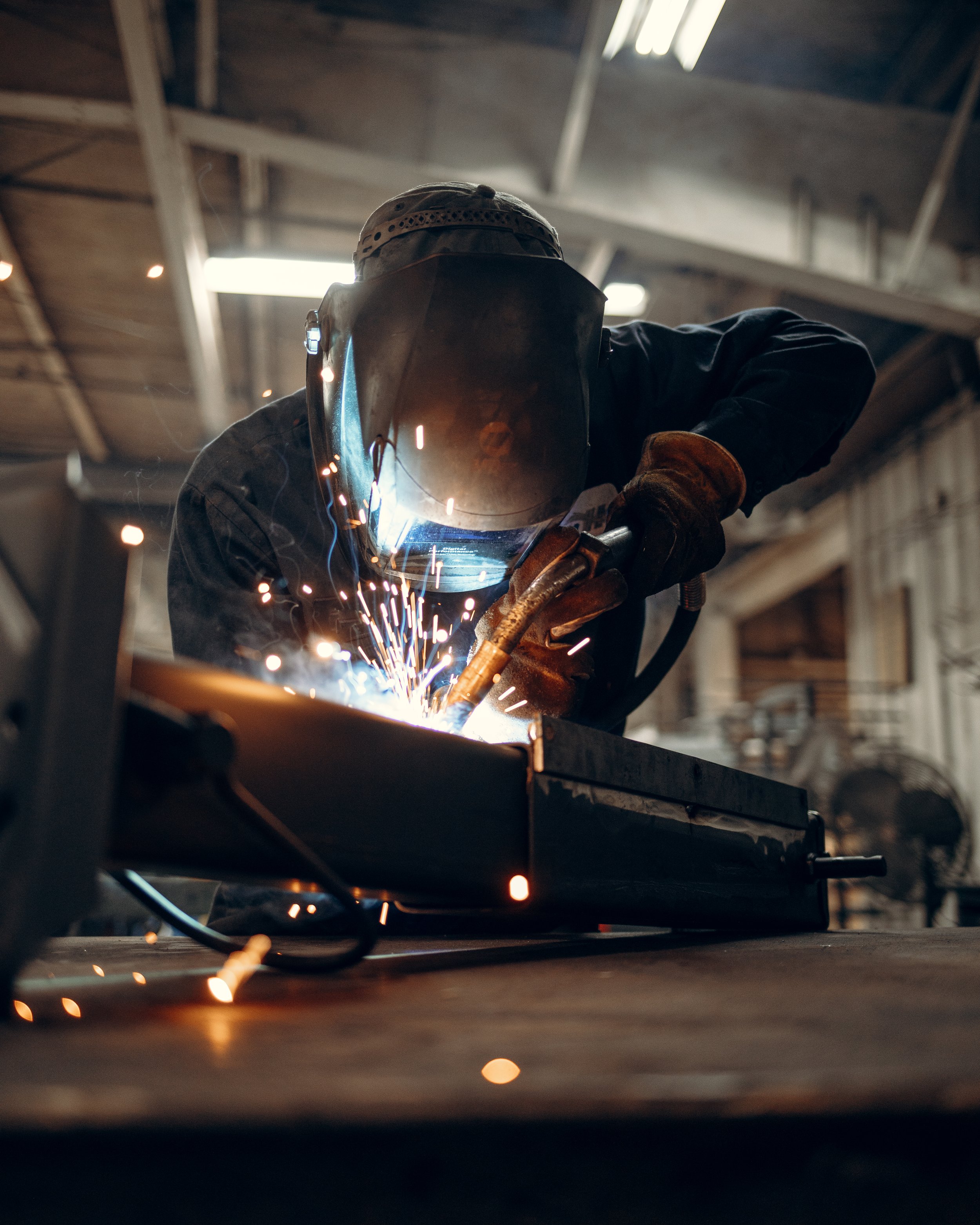 Person welding metal in a workshop, wearing protective gear and helmet, with sparks flying.