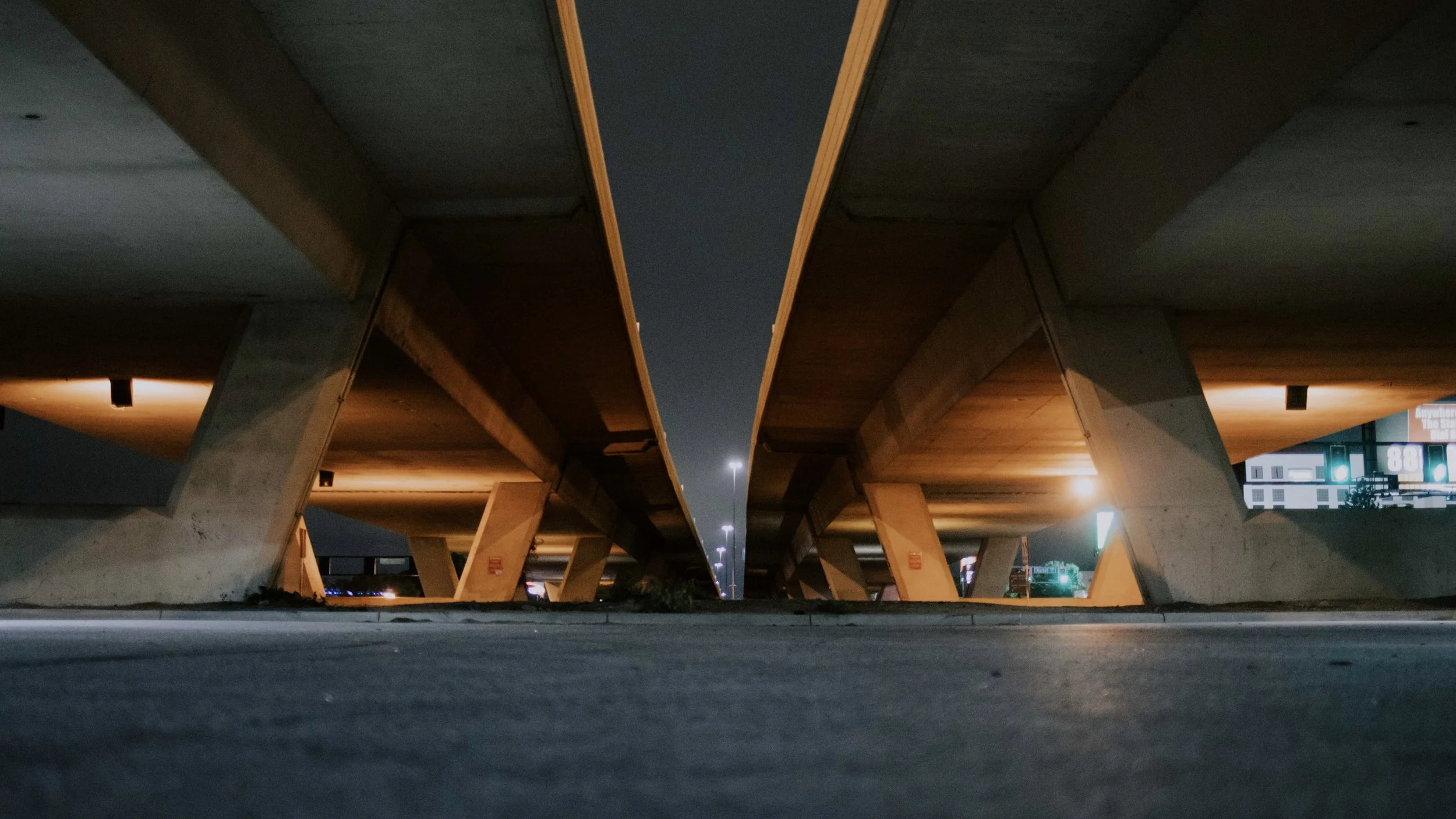 Underneath a highway overpass at night, with lit streetlights and concrete pillars.