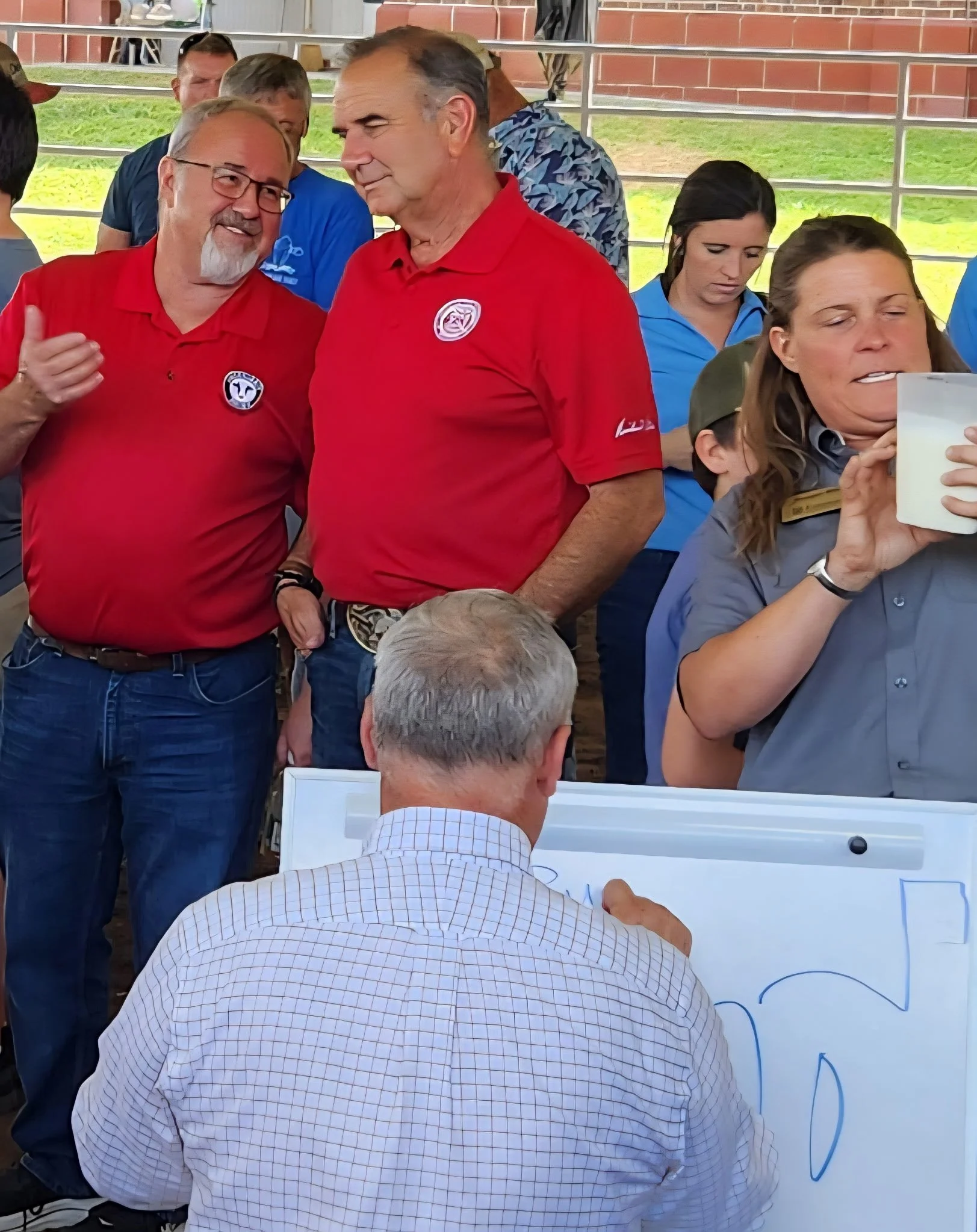 Governor Mike Kehoe watches the cow milking contest as Reagan measures and Alfred records the results.