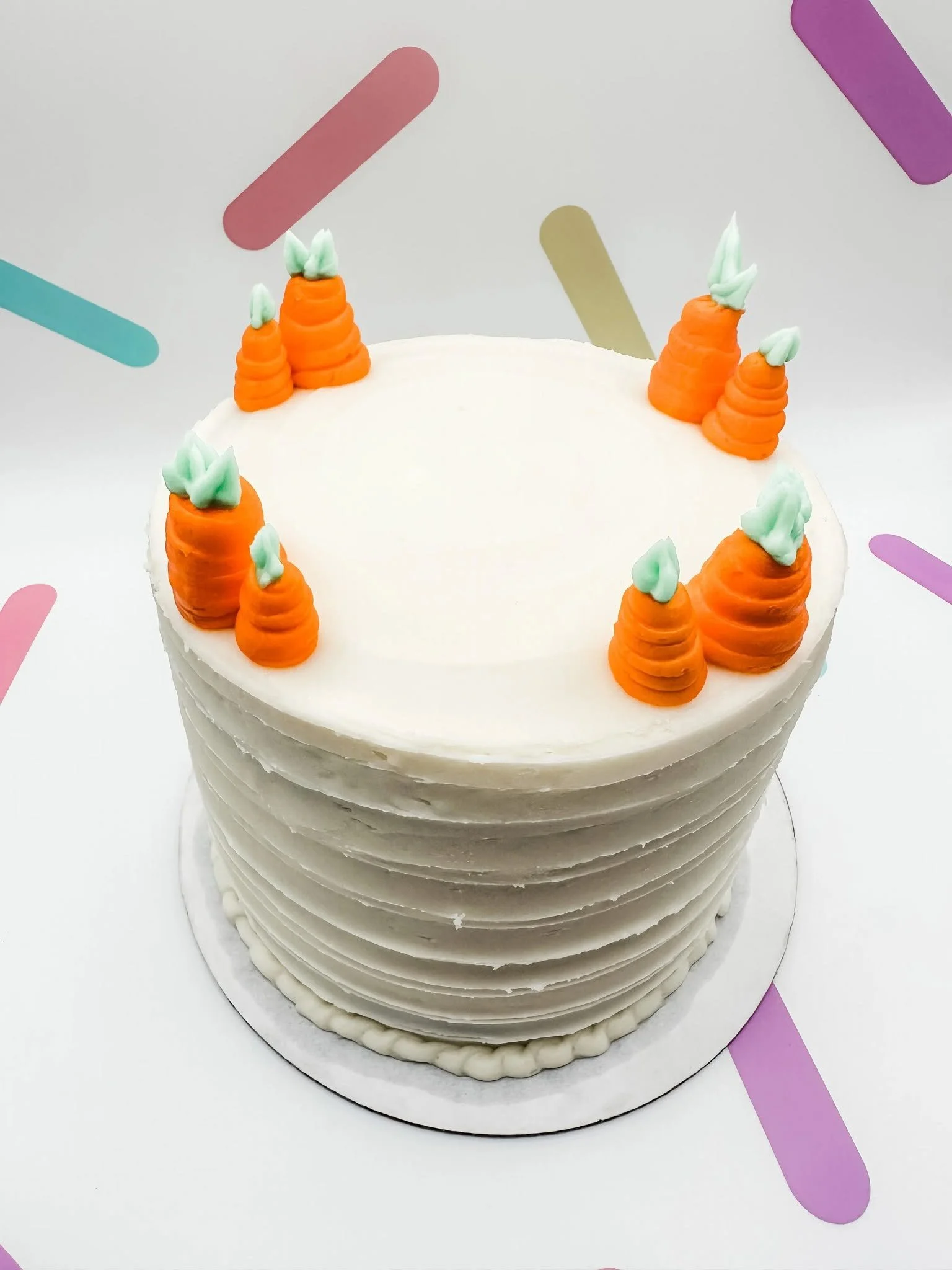 Deb's whole carrot cake with white frosting and orange and green piped carrot decorations.
