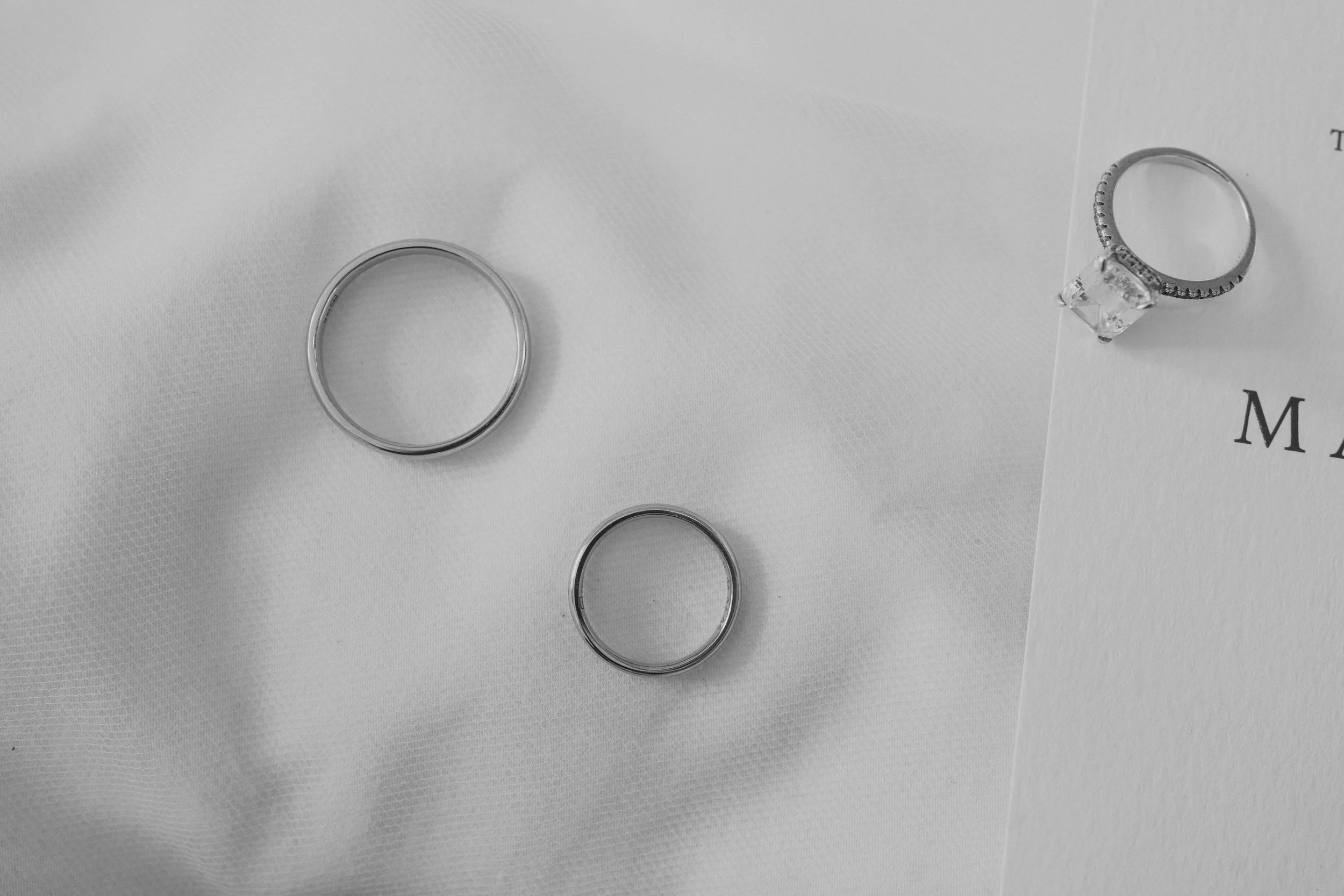 Tres anillos, uno con un diseño simple y dos con un diseño más adornado, colocados sobre tela y papel
