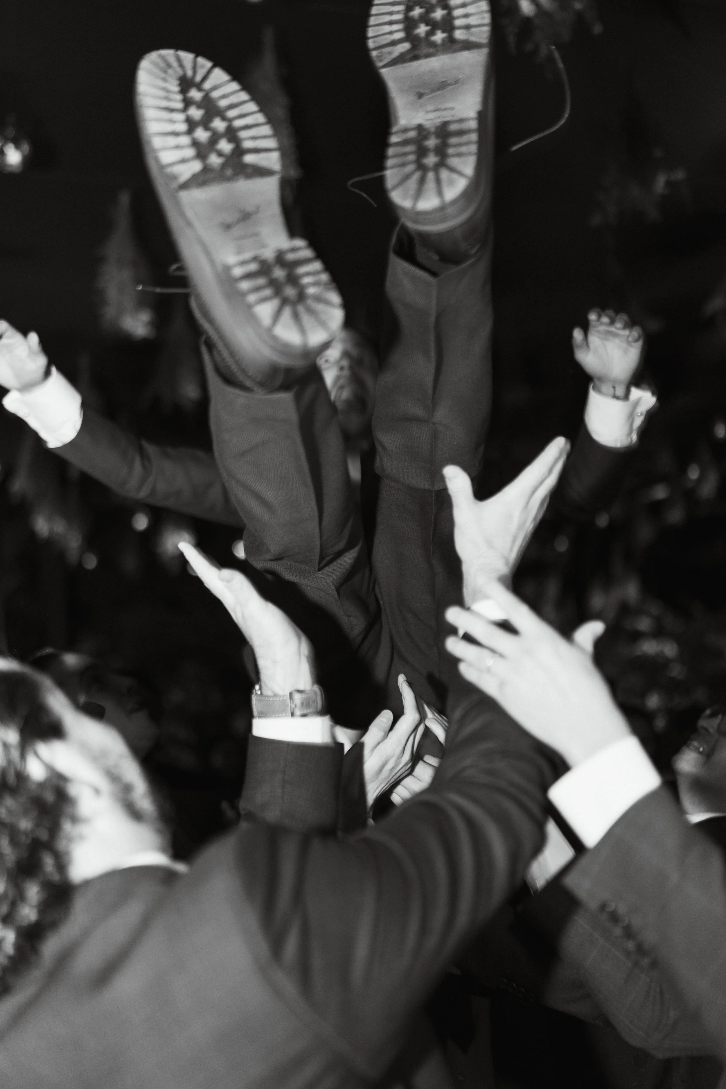 Personas en trajes formales levantando una persona en el aire por las piernas en una celebración