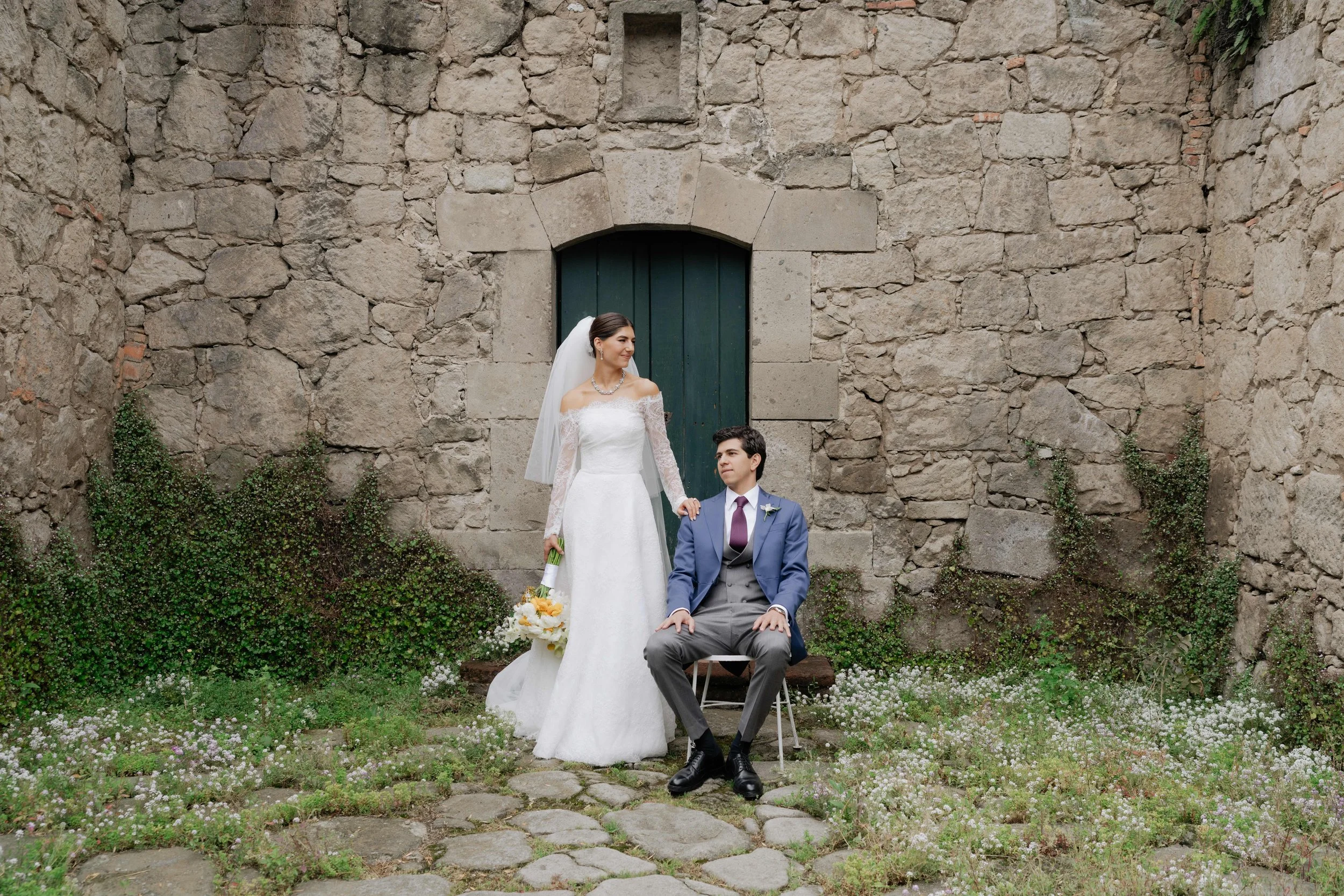 Una pareja de novios en una sesión de fotos de bodas en un entorno rústico con paredes de piedra y plantas verdes.