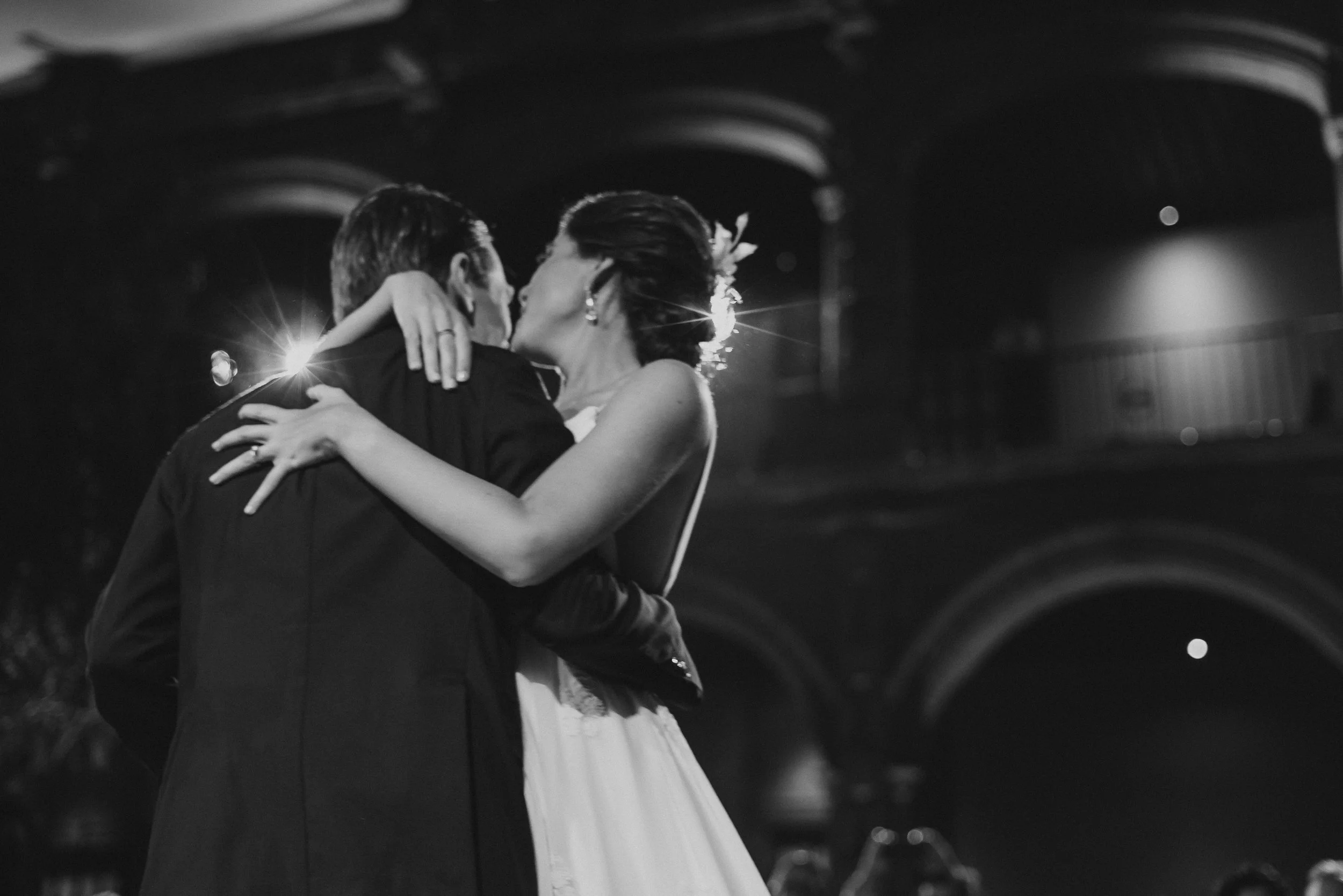 Pareja de novios bailando en su boda en un lugar cerrado, en blanco y negro, en un abrazo y beso romántico.