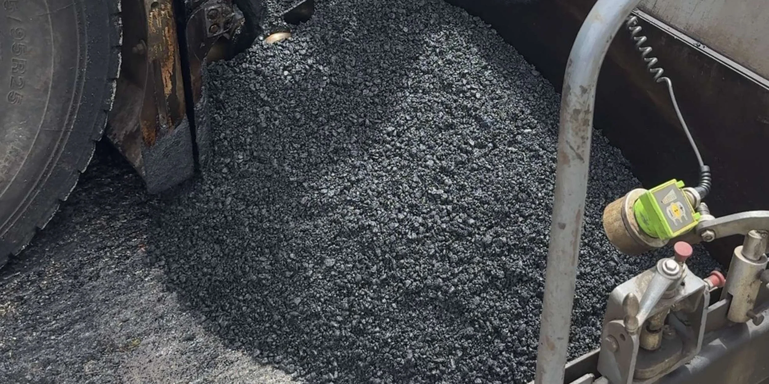 Close-up of hot asphalt mix beside the paver during road surfacing works