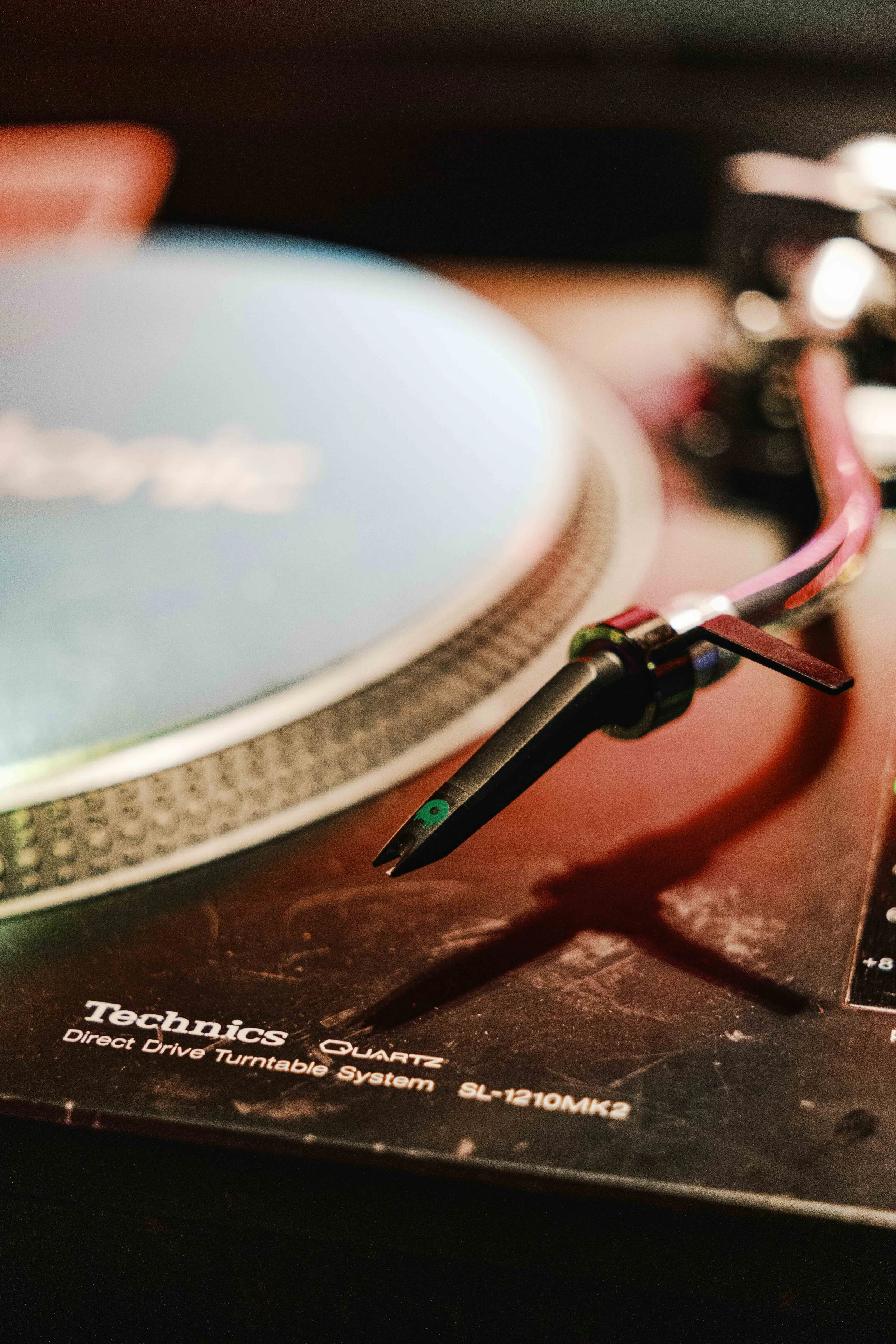 Close-up of a turntable tonearm resting on a record with part of the record label visible, placed on a turntable with visible mechanics.