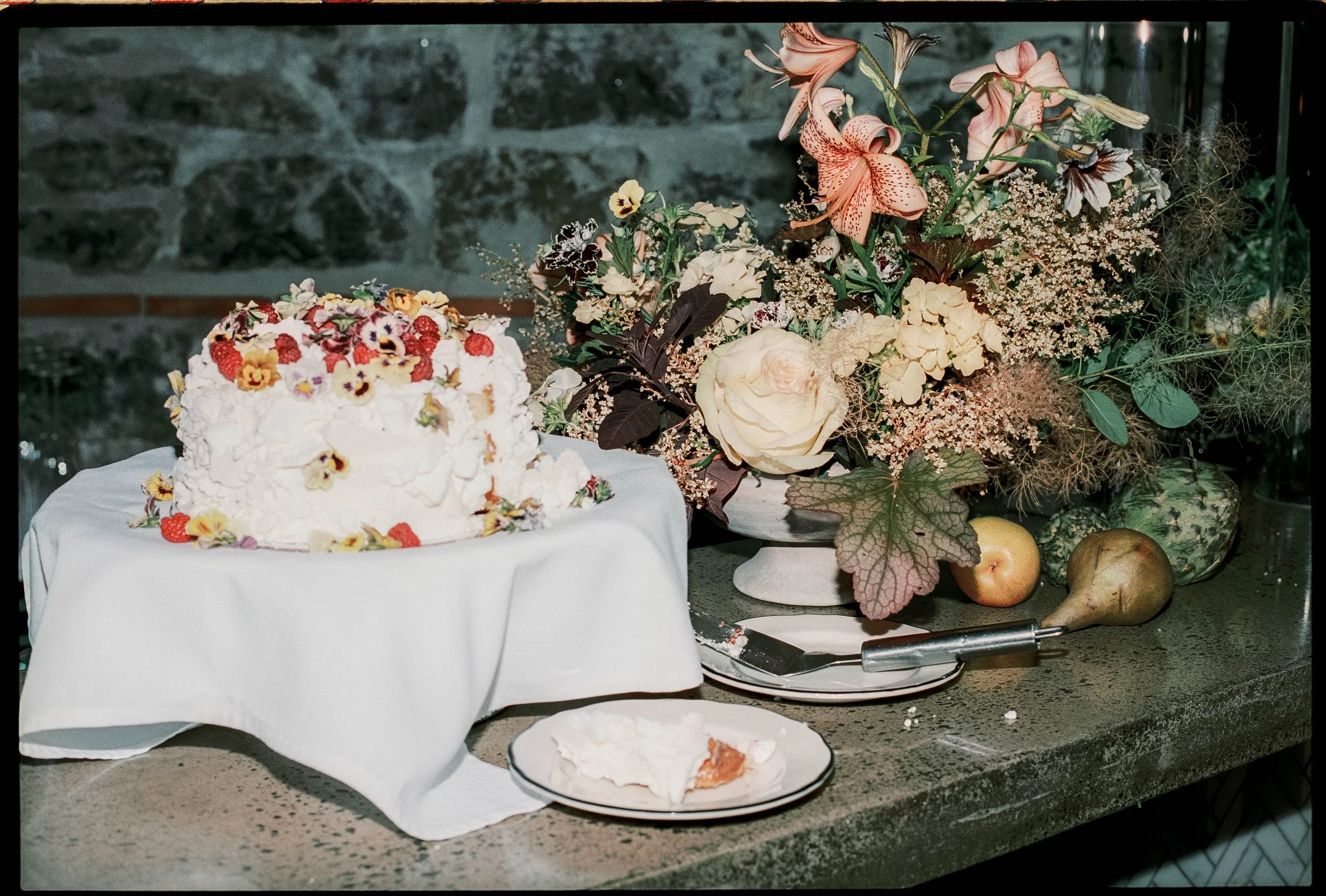 Local cake with fresh flowers and berries next to flower arrangement.