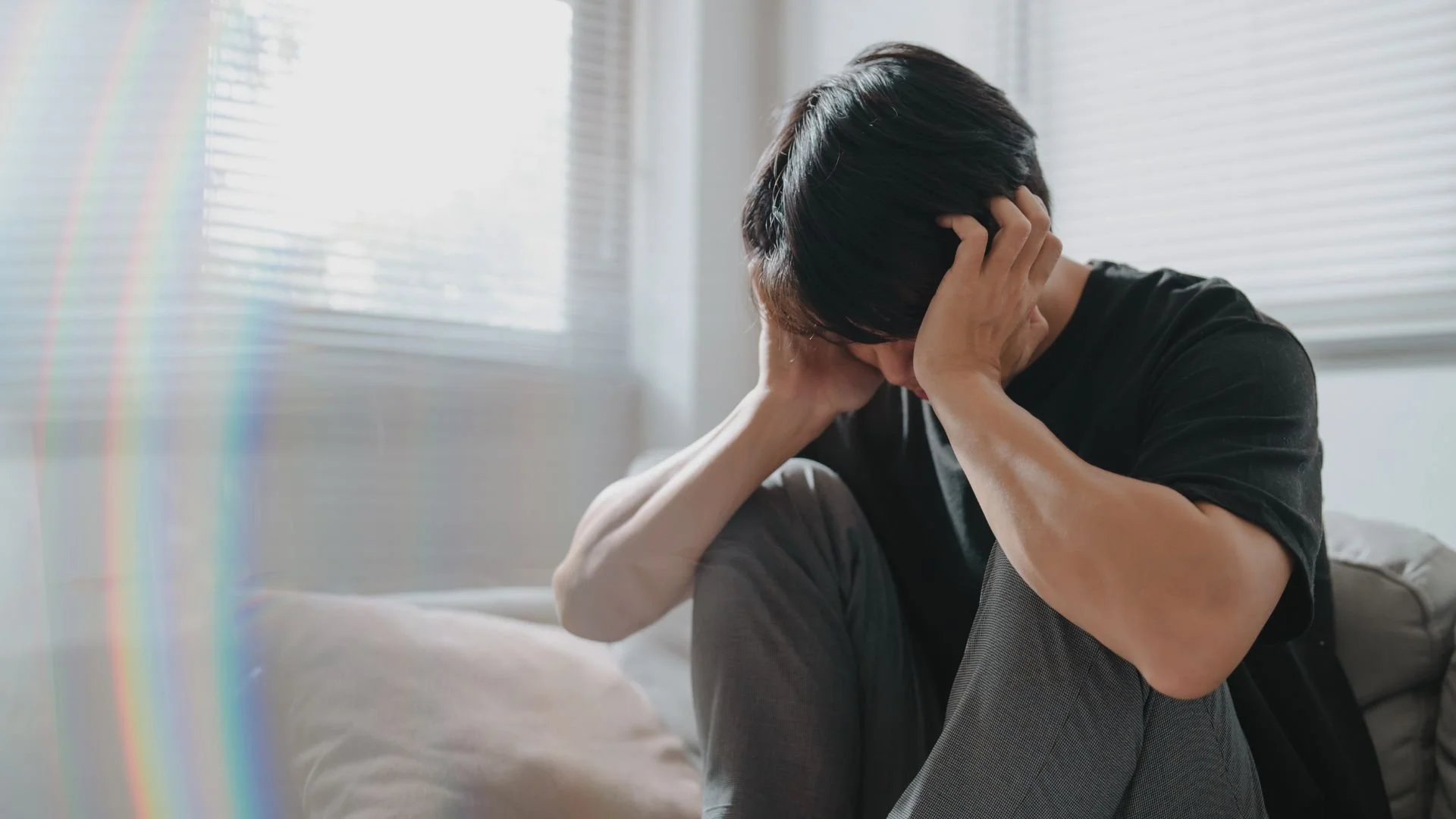 A sad, bearded man sitting alone on a couch, illustrating the symptoms of clinical depression treatable with EMDR therapy.