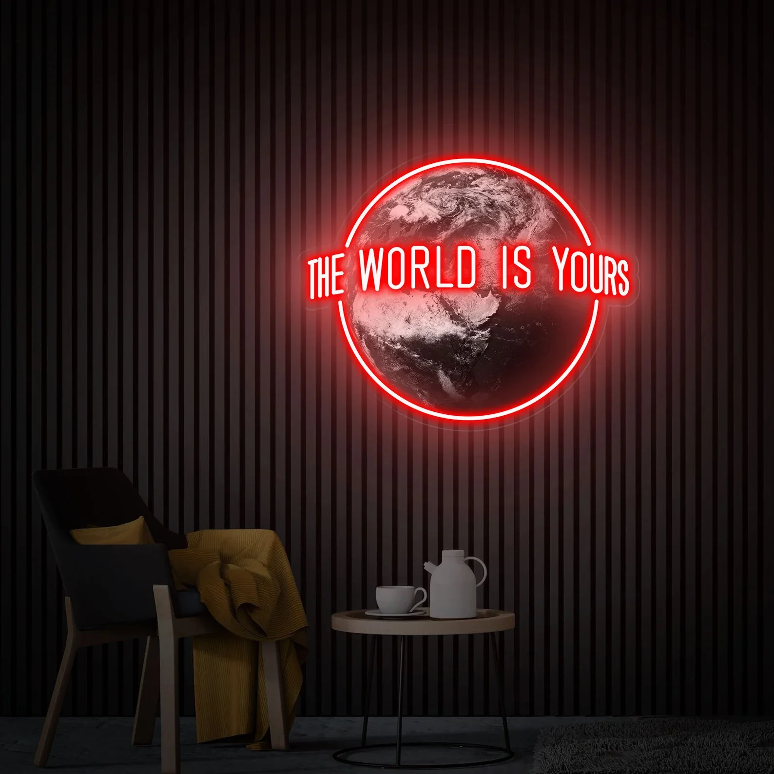 Neon sign of Earth with the phrase 'The World Is Yours' in red, illuminated against a dark, vertically striped wall. Nearby, a chair with a yellow blanket and pillow, and a small round table with a white teapot and cup.