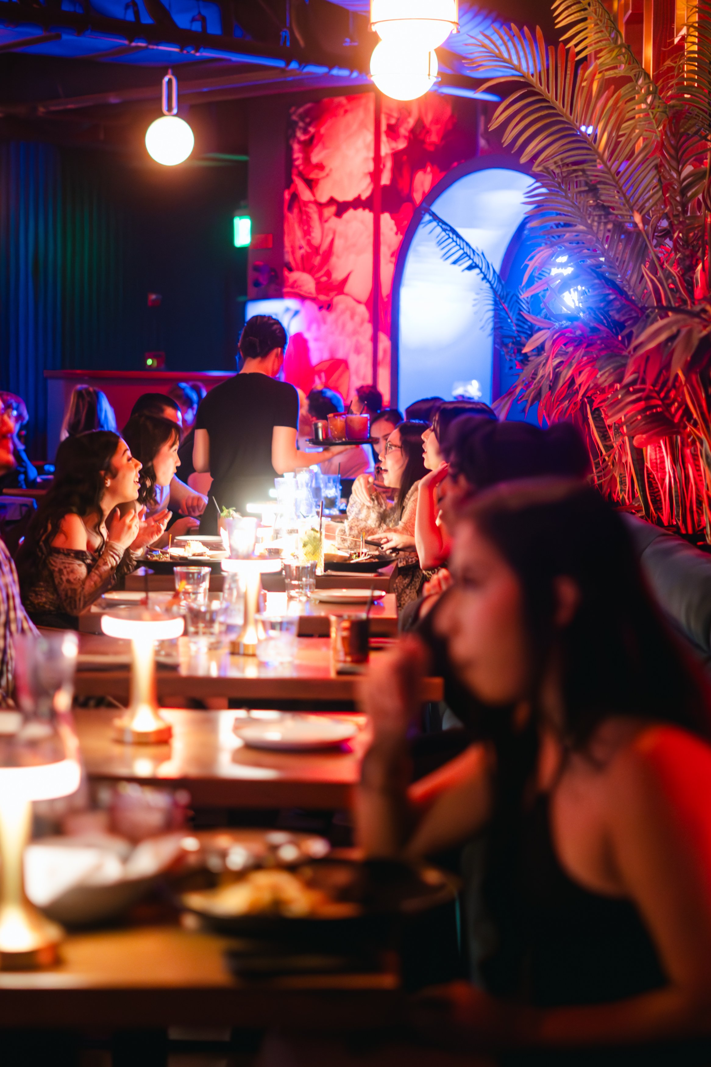 People dining at a lively restaurant with colorful lighting and cozy ambiance.