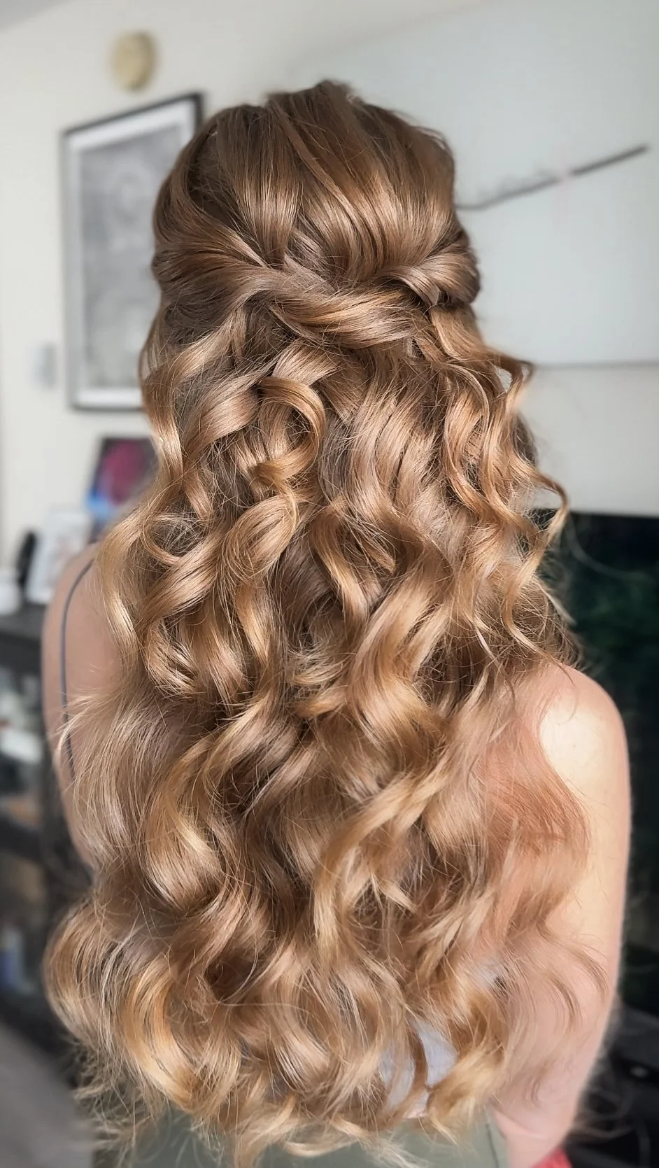 Back view of a woman with long, blonde, curly hair styled with half-up twist.