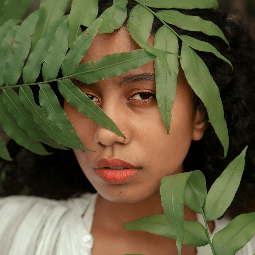 A black woman peeking from behind some leaves.